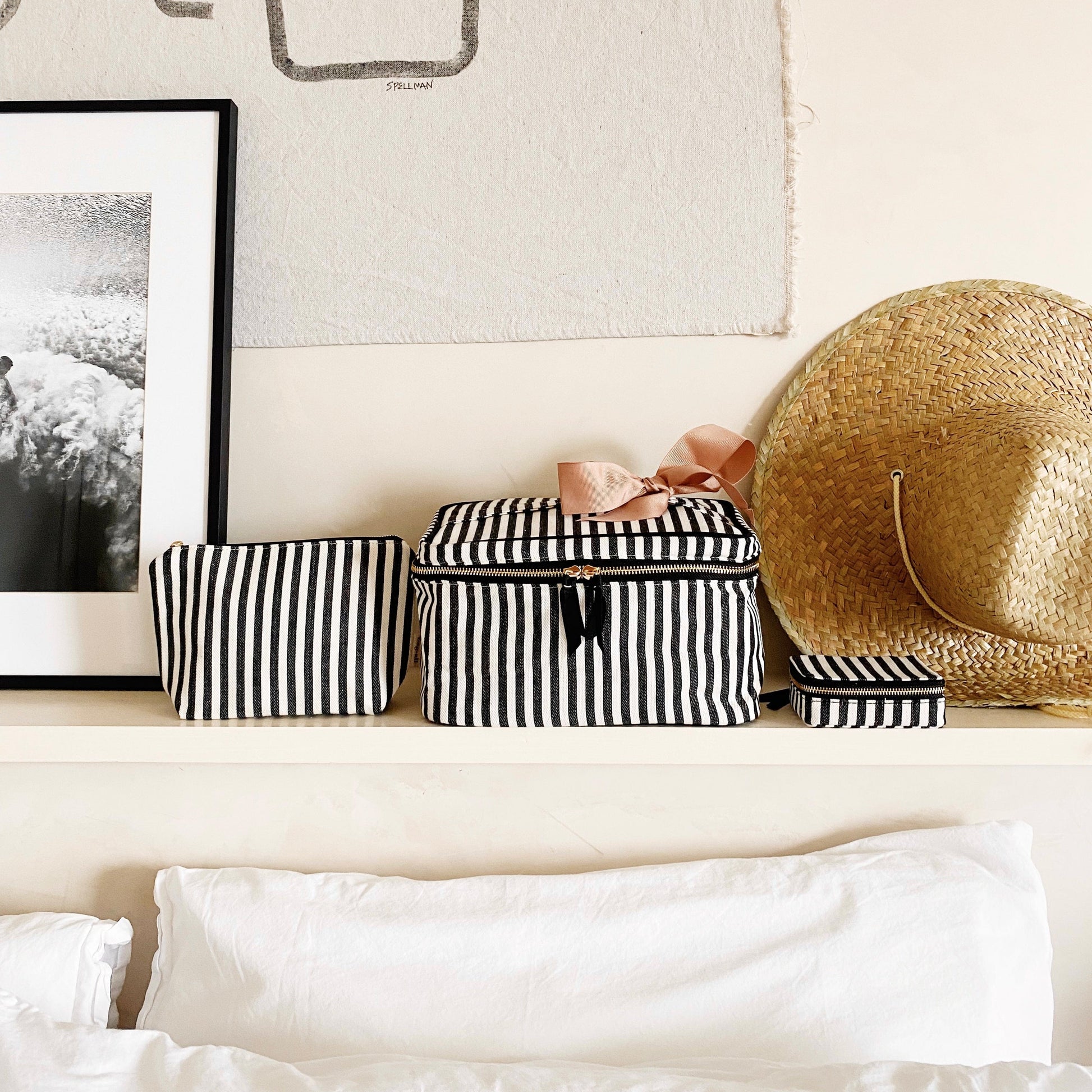 Bag-all Cutest Striped Travel Gift Set 3-Pack featuring black and white striped cotton makeup bag, toiletry case, and pill organizer displayed on white shelf with straw hat and framed artwork