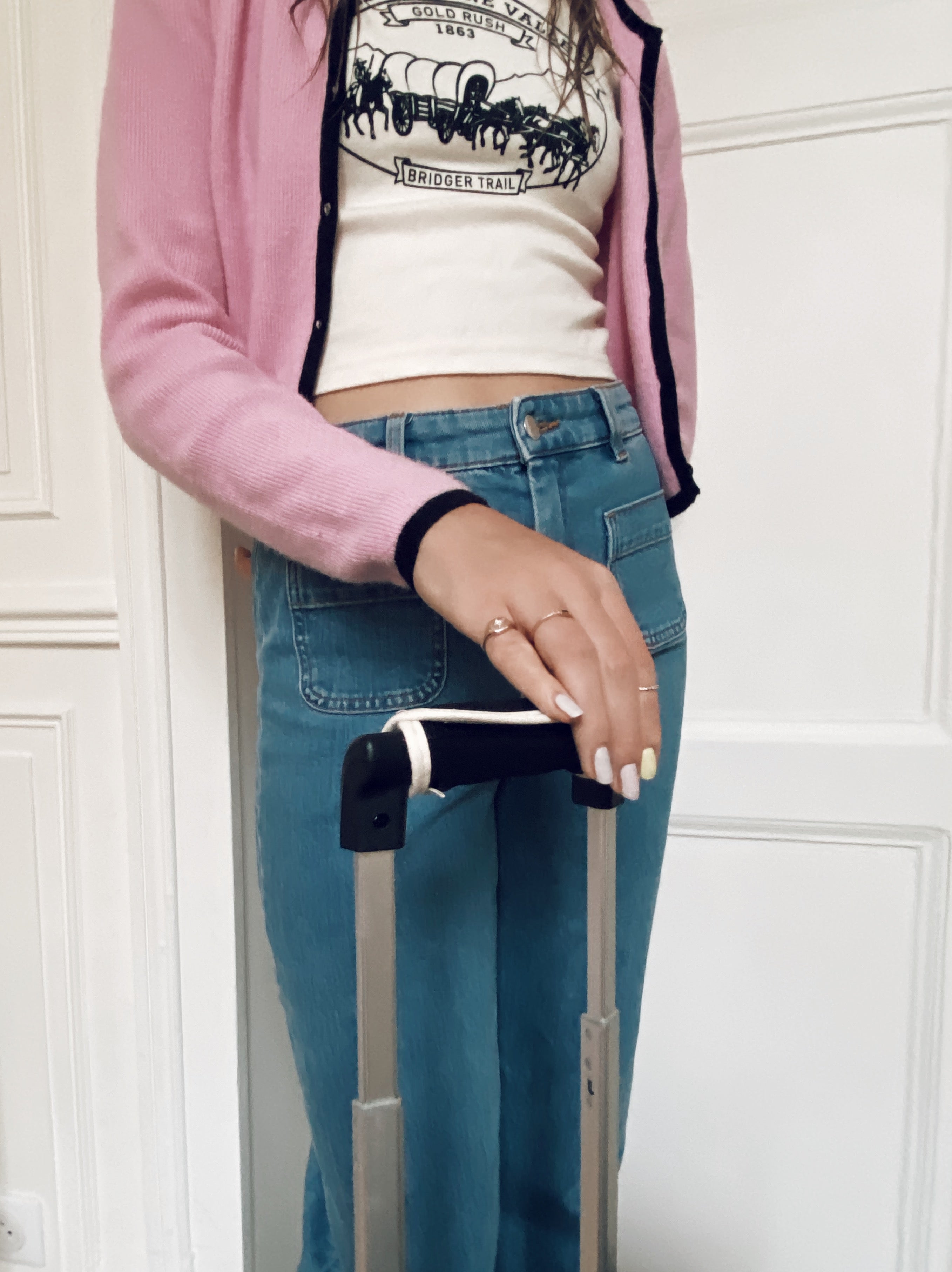 Bag-all Luggage Handle Cover in black neoprene shown on metal suitcase handle, demonstrated by person wearing pink cardigan and jeans, highlighting comfortable grip and practical travel accessory design