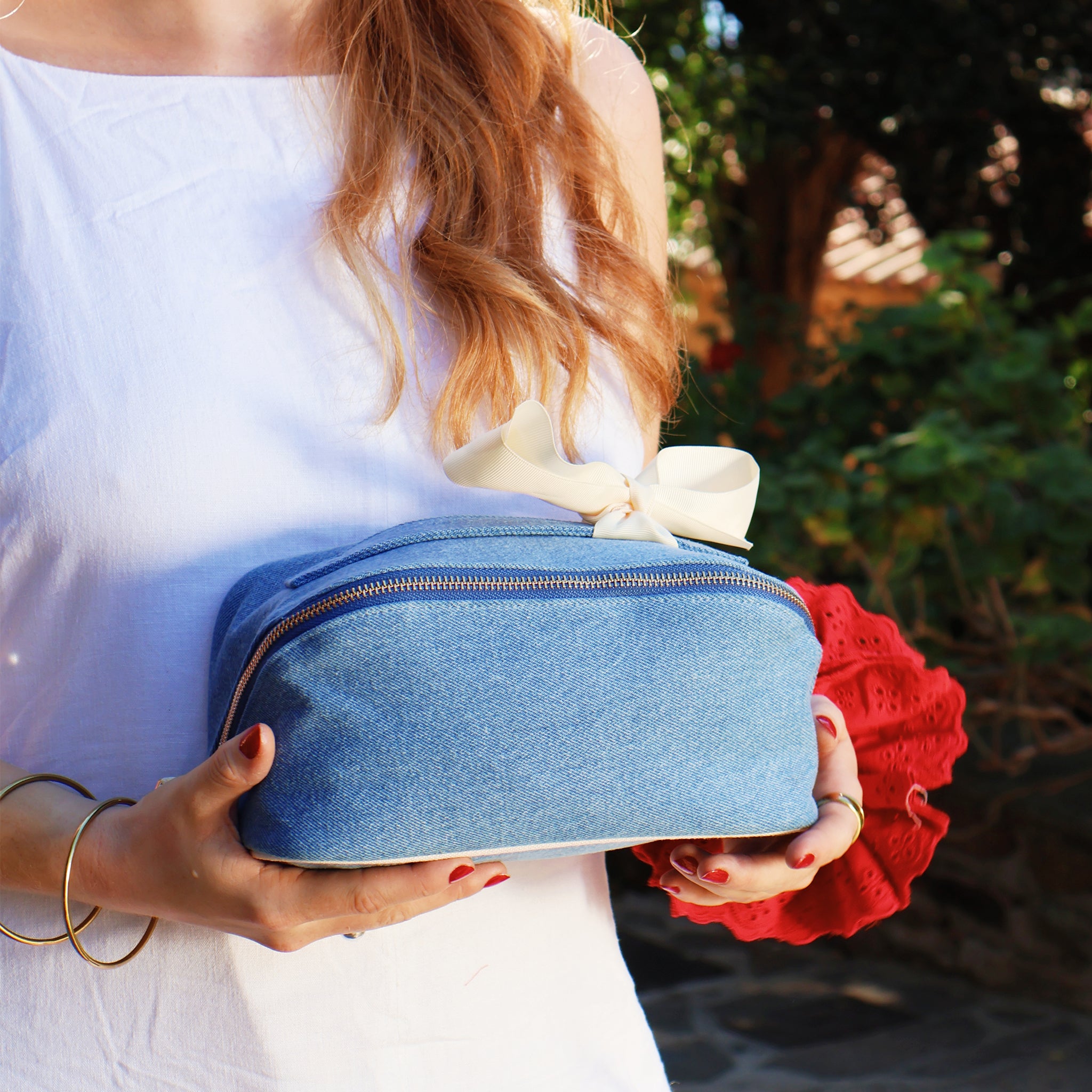 Woman holding a denim Accordion Box makeup and toiletry organizer by Bag-all with striped interior and elegant bow detail