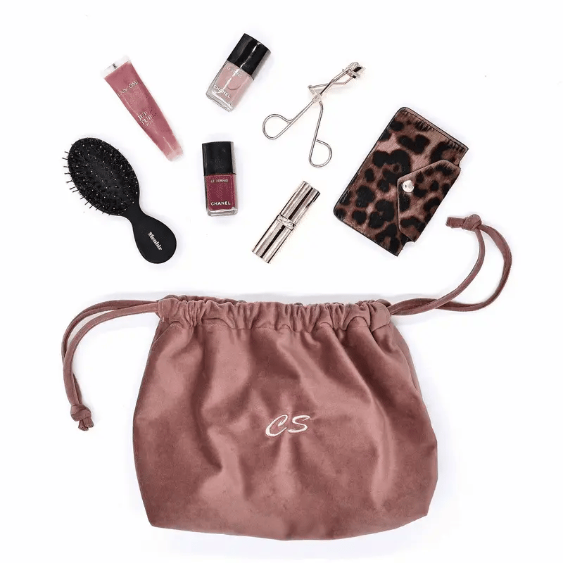 Pink velvet drawstring makeup organizing bag by Bag-all with cosmetics and accessories neatly arranged nearby.