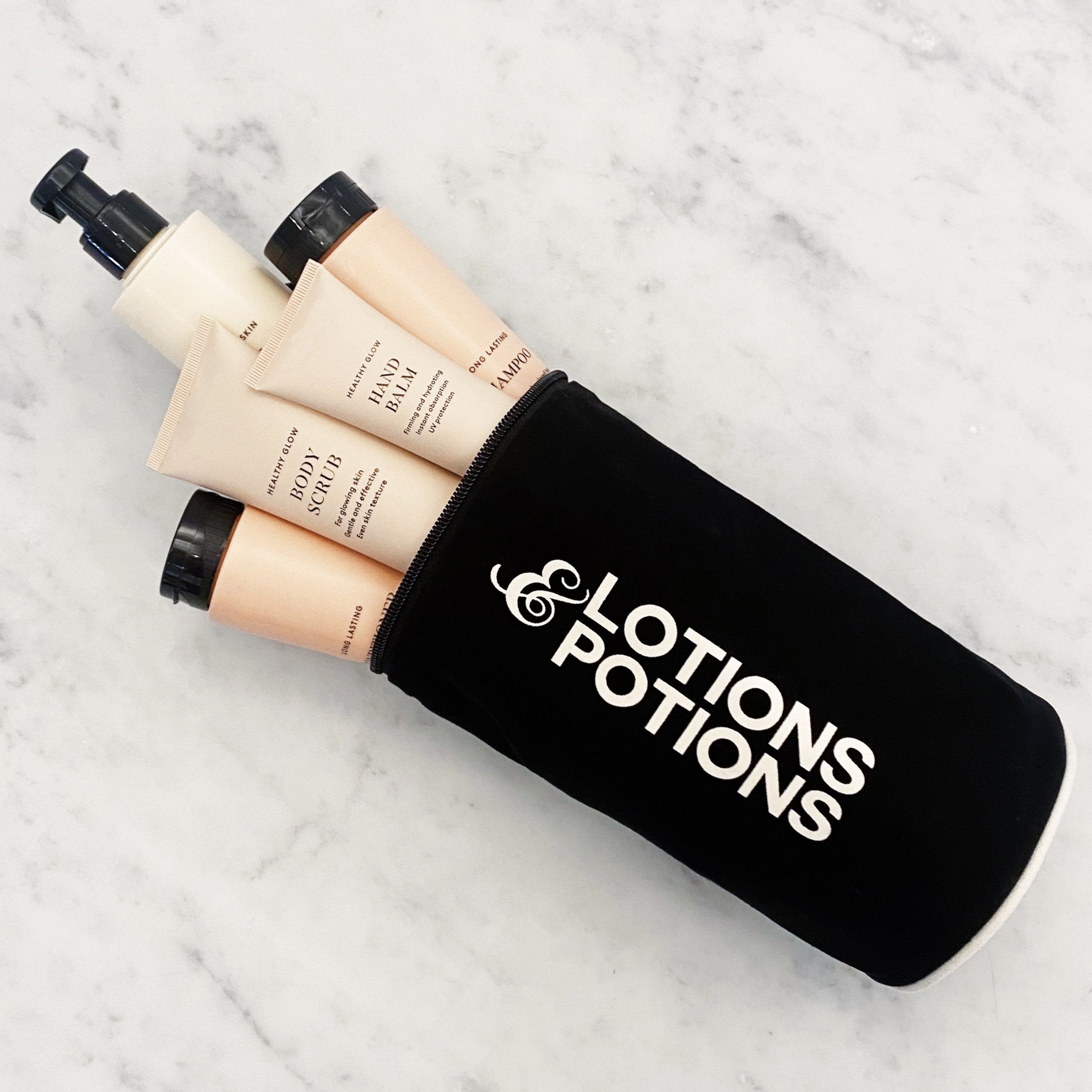 Bag-all black velvet cosmetic pouch with white Lotions & Potions text holding skincare tubes on marble surface
