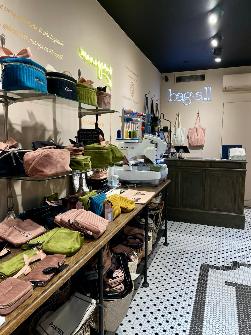 Bag-all display of colorful pouches and bags on shelves with sewing machine and neon logo inside store gallery position 1
