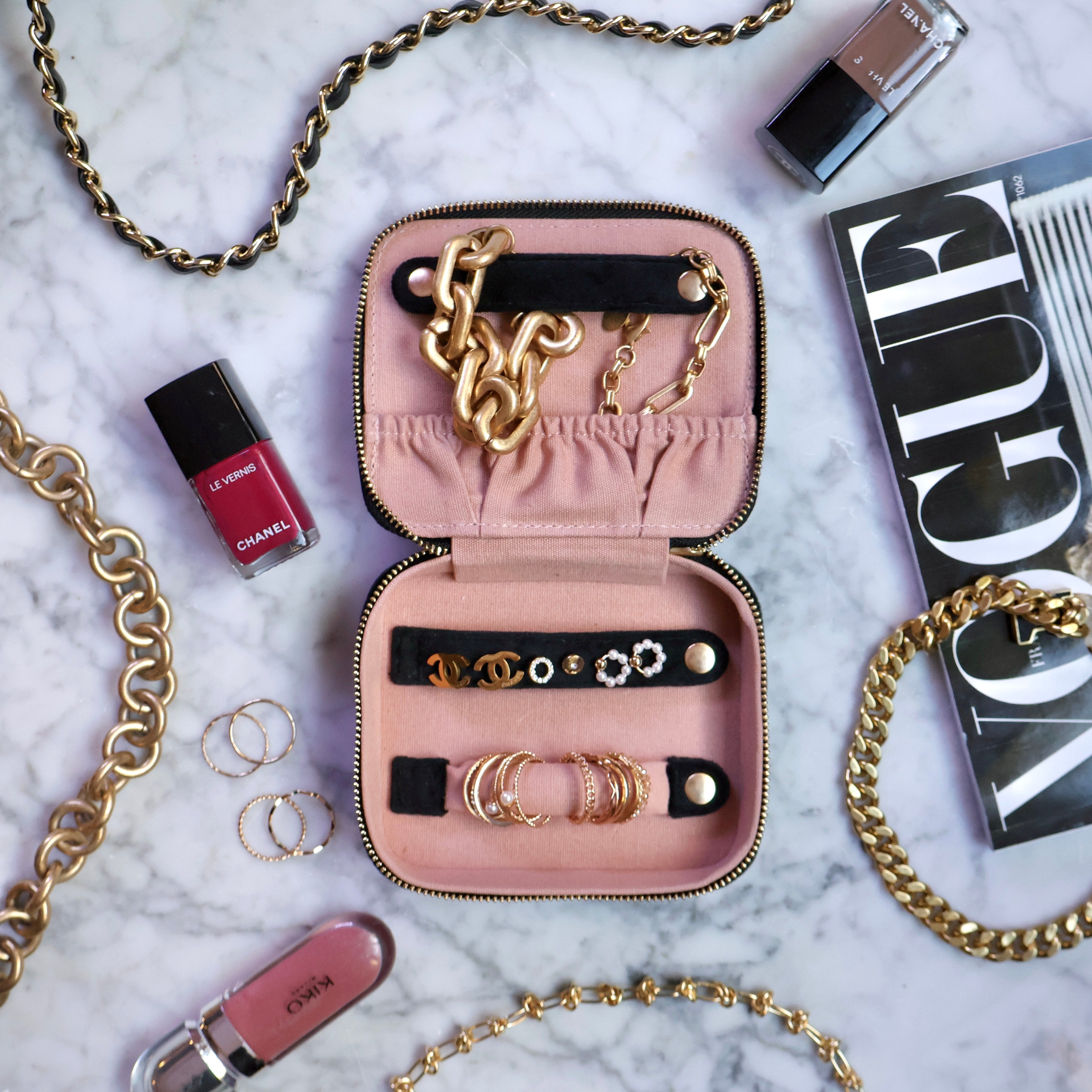 Pink velvet Bag-all Cute Jewelry Box open with gold chains, earrings, and rings on marble with cosmetics nearby