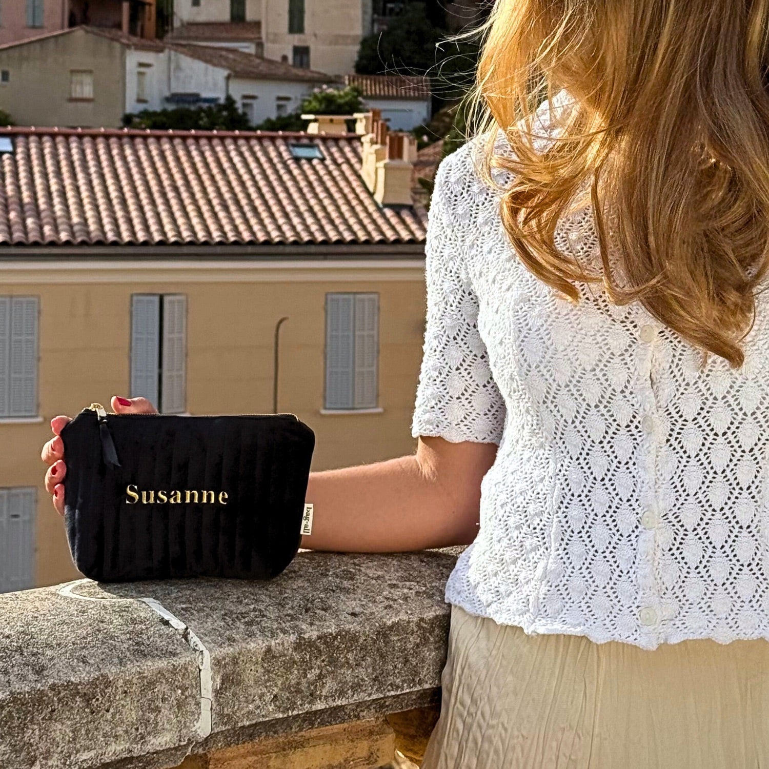 Woman holding a personalized quilted black velvet makeup pouch with coated lining by Bag-all outdoors on stone wall