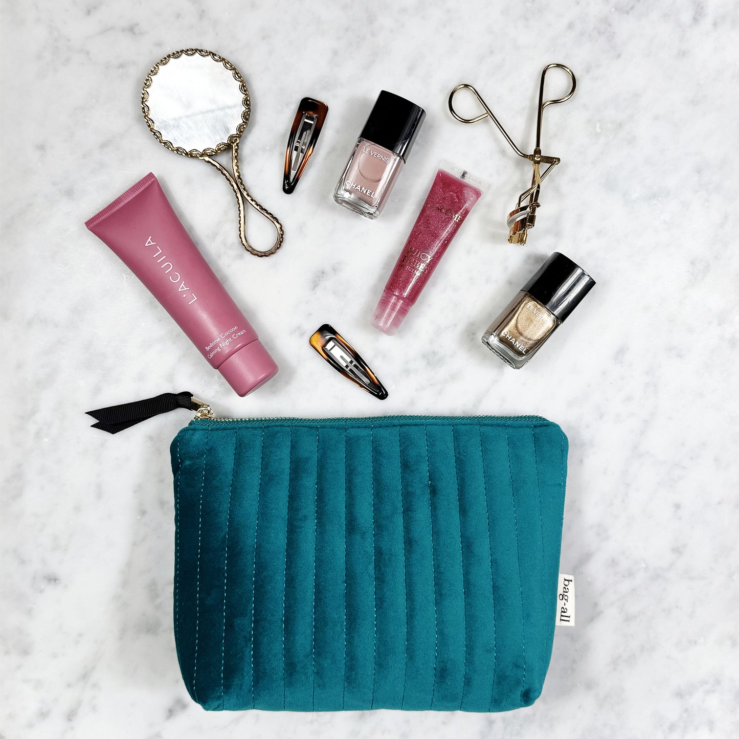 Quilted teal velvet makeup pouch with coated lining by Bag-all holding beauty essentials on marble surface.