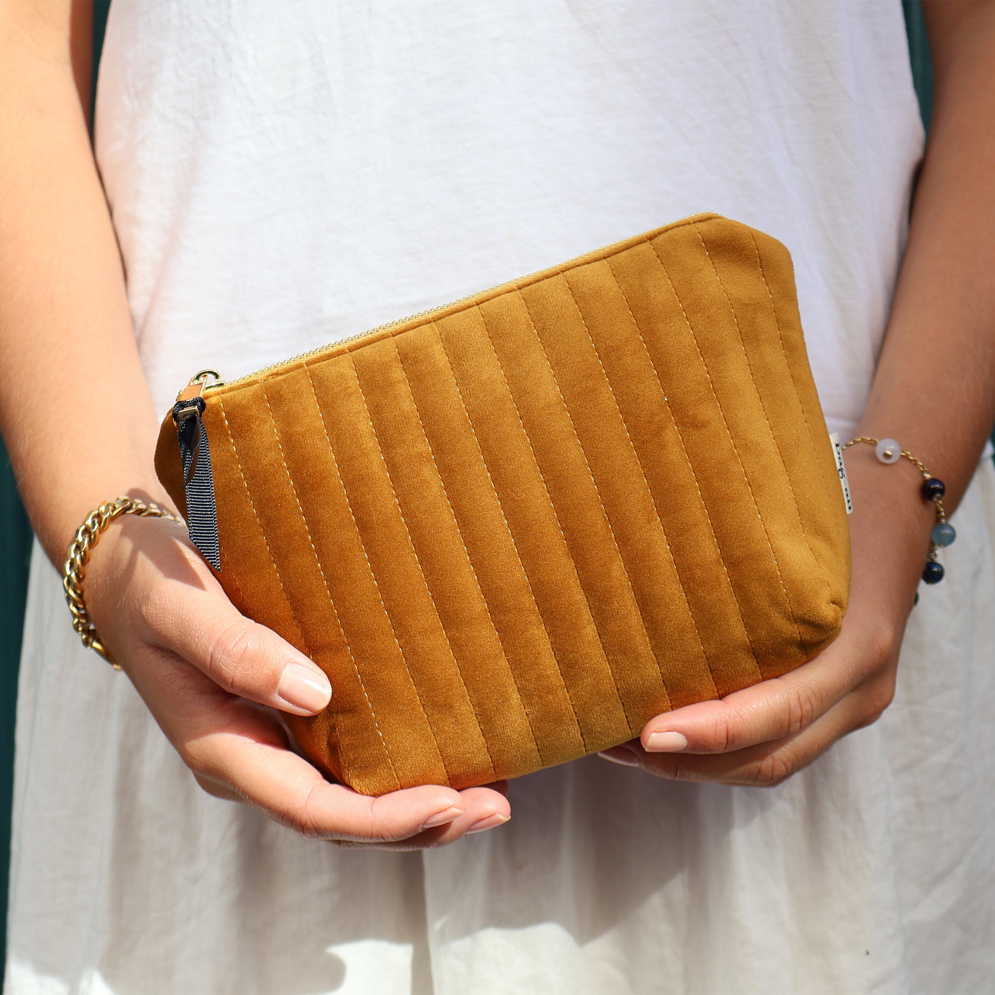 Hands holding a quilted yellow velvet makeup pouch with coated lining by Bag-all against white dress background