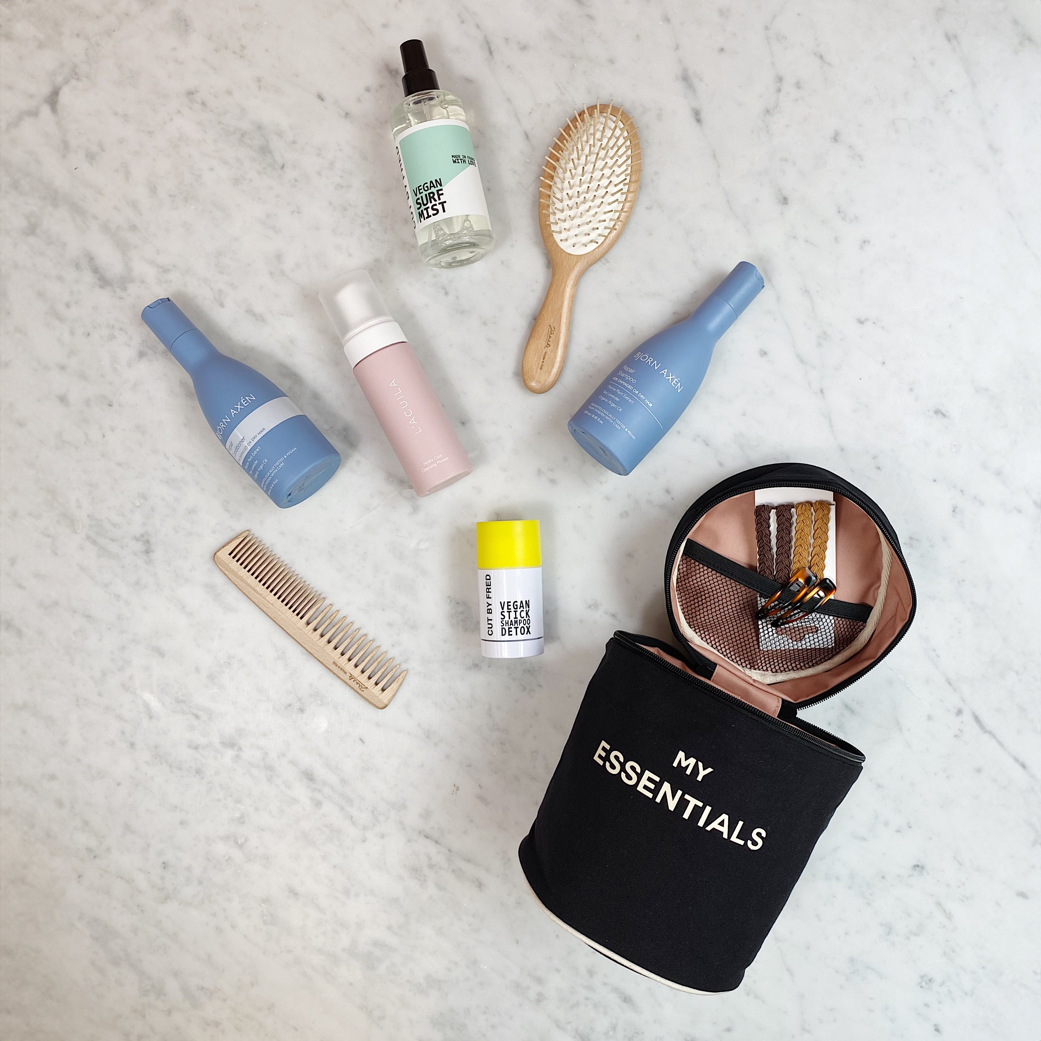 Bag-all Round My Essentials Case in black displayed with beauty products, hairbrush, and toiletries on marble surface, showcasing its spacious interior and practical organization features