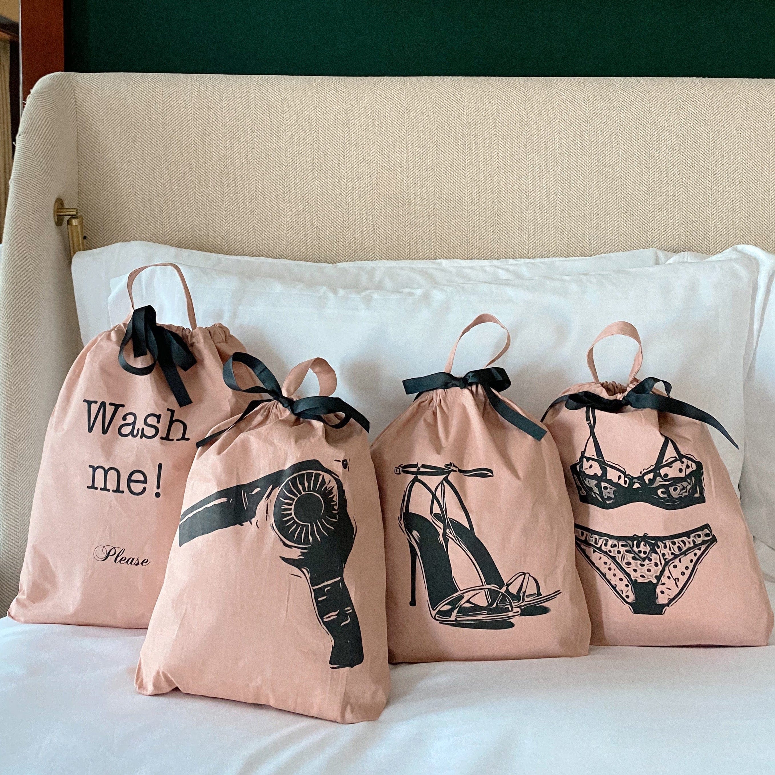 Bag-all Women's Travel Set 4-pack in pink/blush featuring laundry, hair dryer, lingerie, and shoe organizer bags with black ribbon ties and stylish graphic prints, displayed on white bedding
