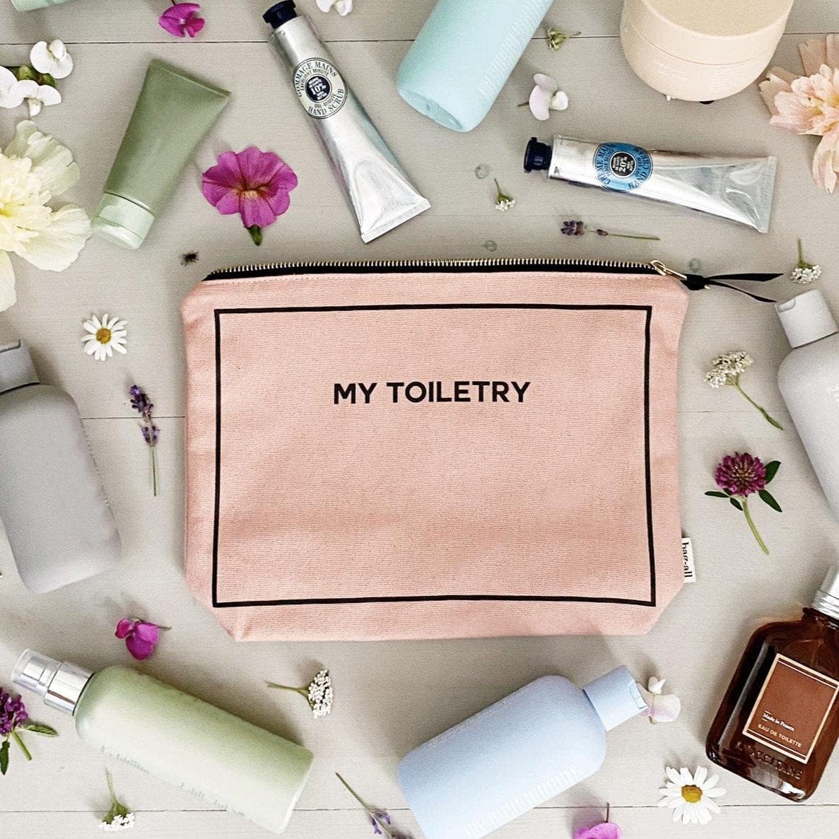 Bag-all Toiletry Travel Gift Set 4-Pack in pink blush cotton featuring My Toiletry pouch surrounded by beauty products and flowers on gray background, perfect for travel organization