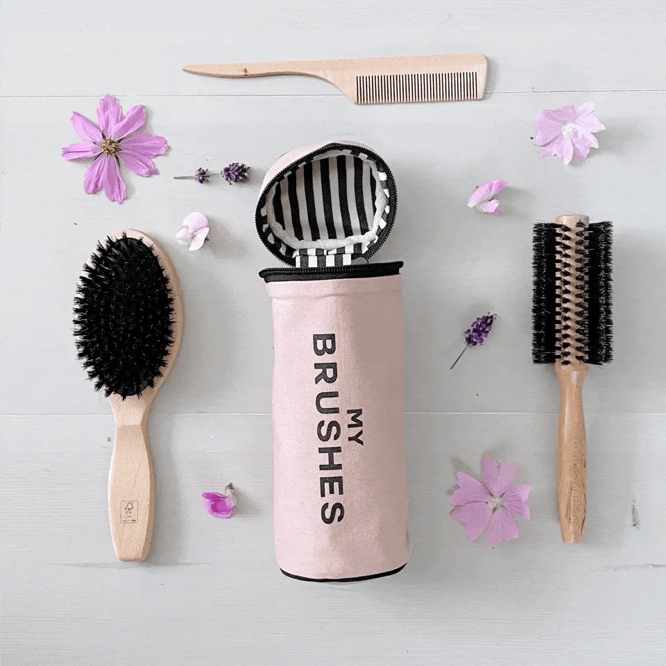Bag-all Pink Cylinder Brushes Case with striped interior, displayed with wooden hair brushes and pink flowers on light gray surface, perfect for organizing beauty tools