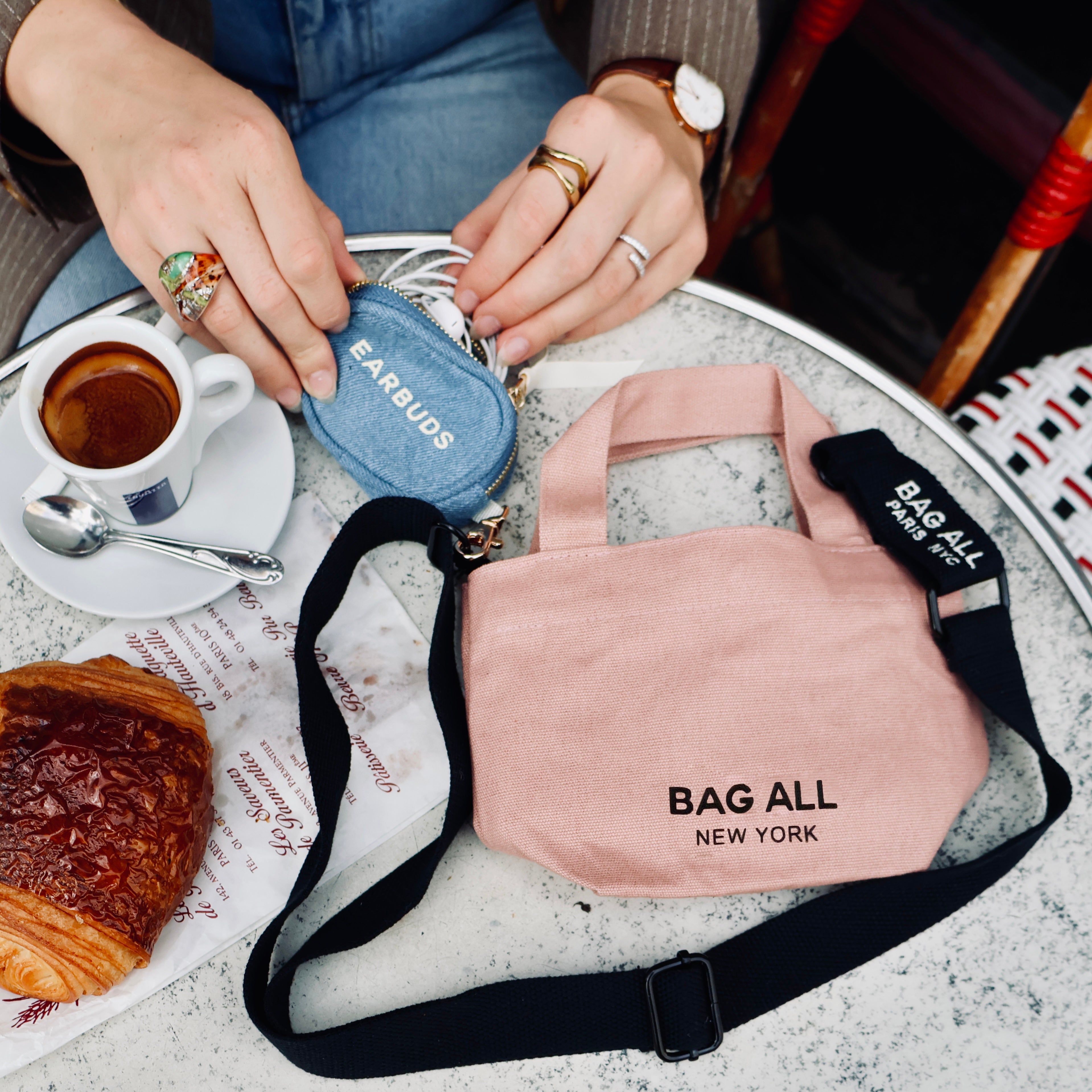 Bag-all Mini Tote Bag in blush pink with black strap, shown on marble table with coffee and croissant, featuring New York branding and compact design for everyday essentials