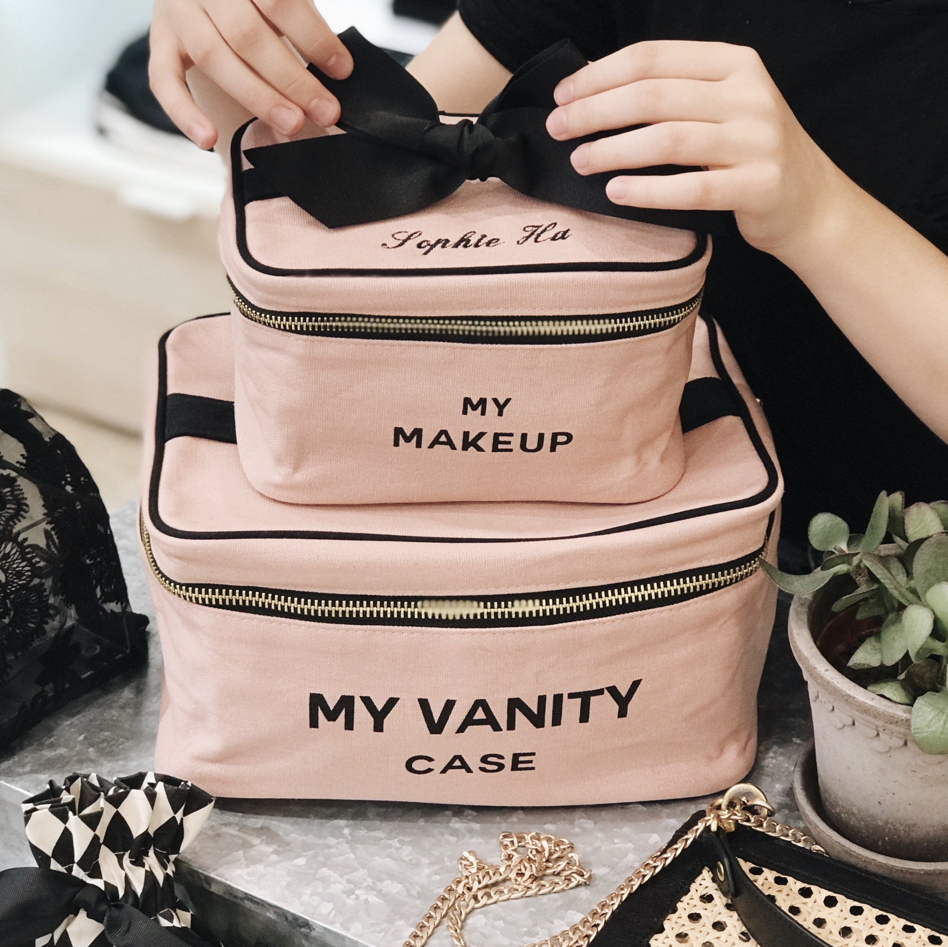 Bag-all My Makeup Cosmetic Box in blush pink with black bow, gold zipper, and personalized text. Stylish vanity case with laminated interior for easy cleaning and organized makeup storage.