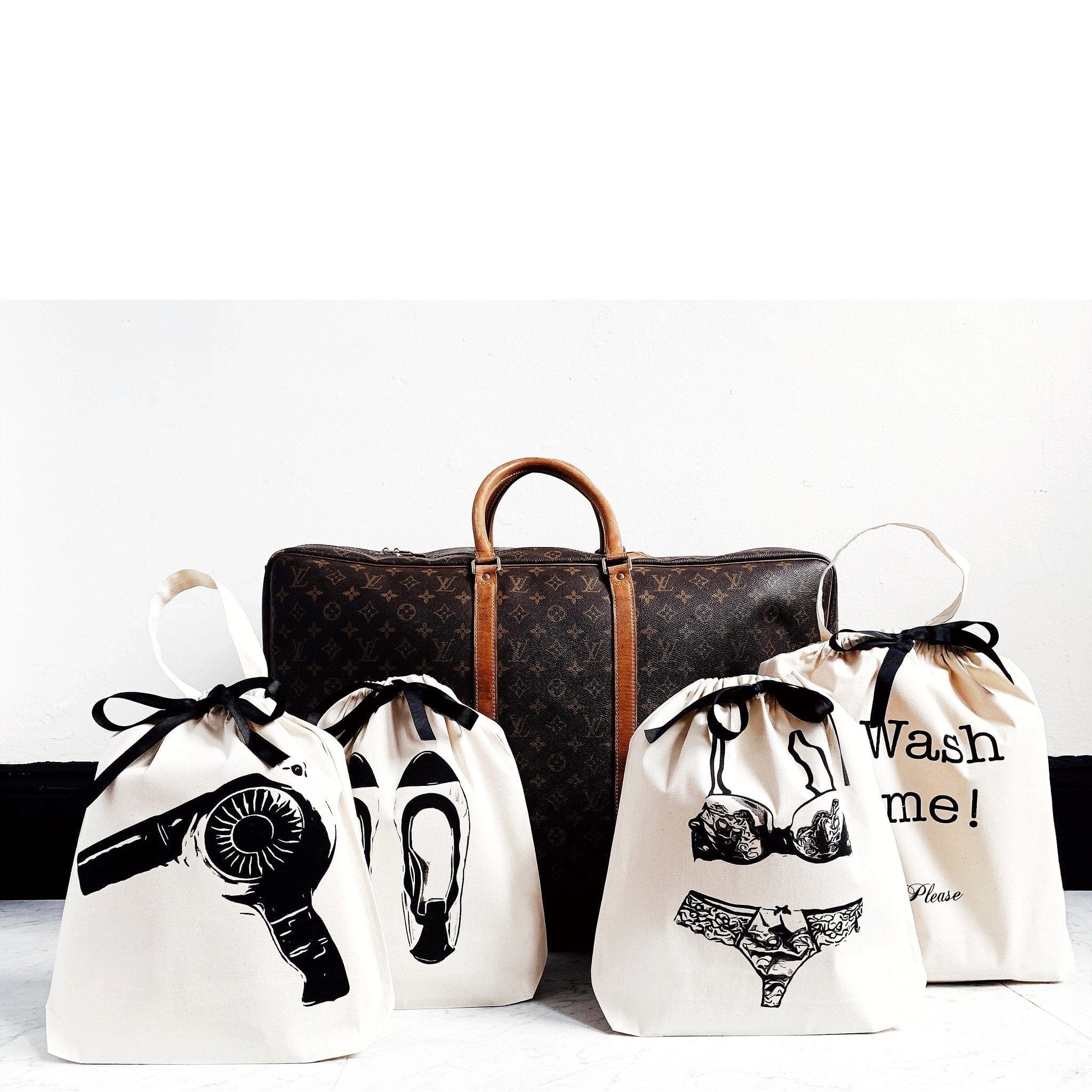 Bag-all Women's Travel Set 4-pack in cream featuring organized travel bags for laundry, hairdryer, lingerie, and ballet flats, displayed with vintage designer luggage