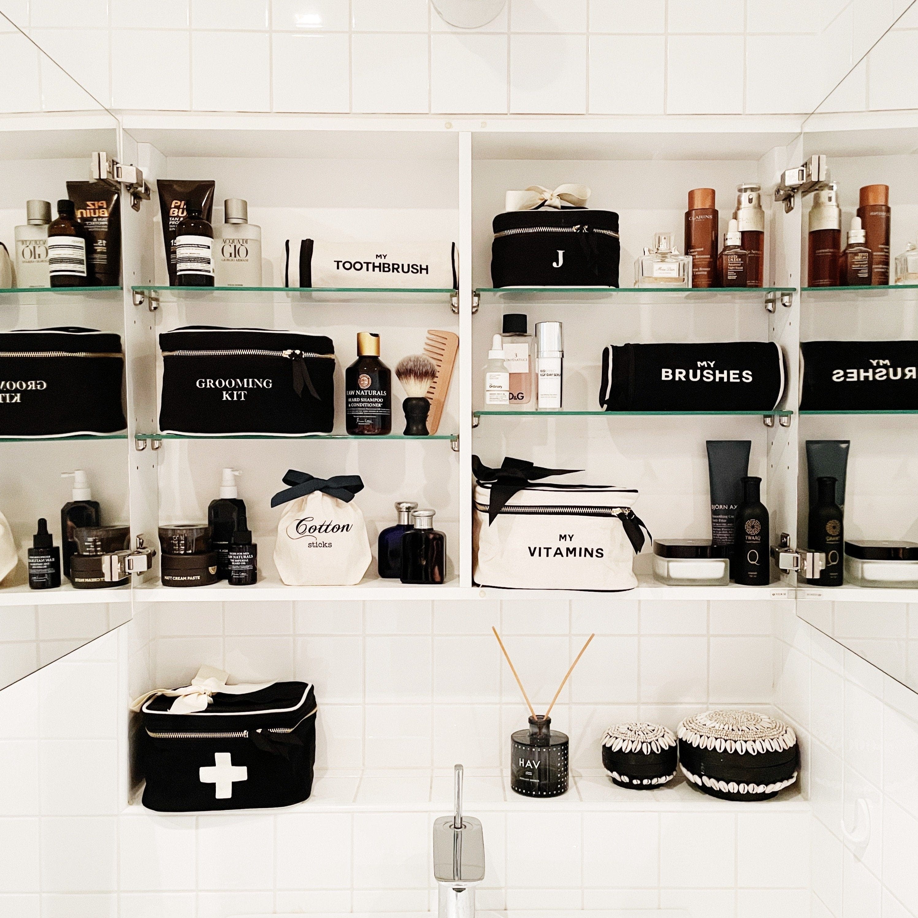 Bag-all Vitamins Storage and Travel Box in cream color displayed in an organized bathroom shelf alongside other black and white toiletry cases and grooming essentials for stylish bathroom organization