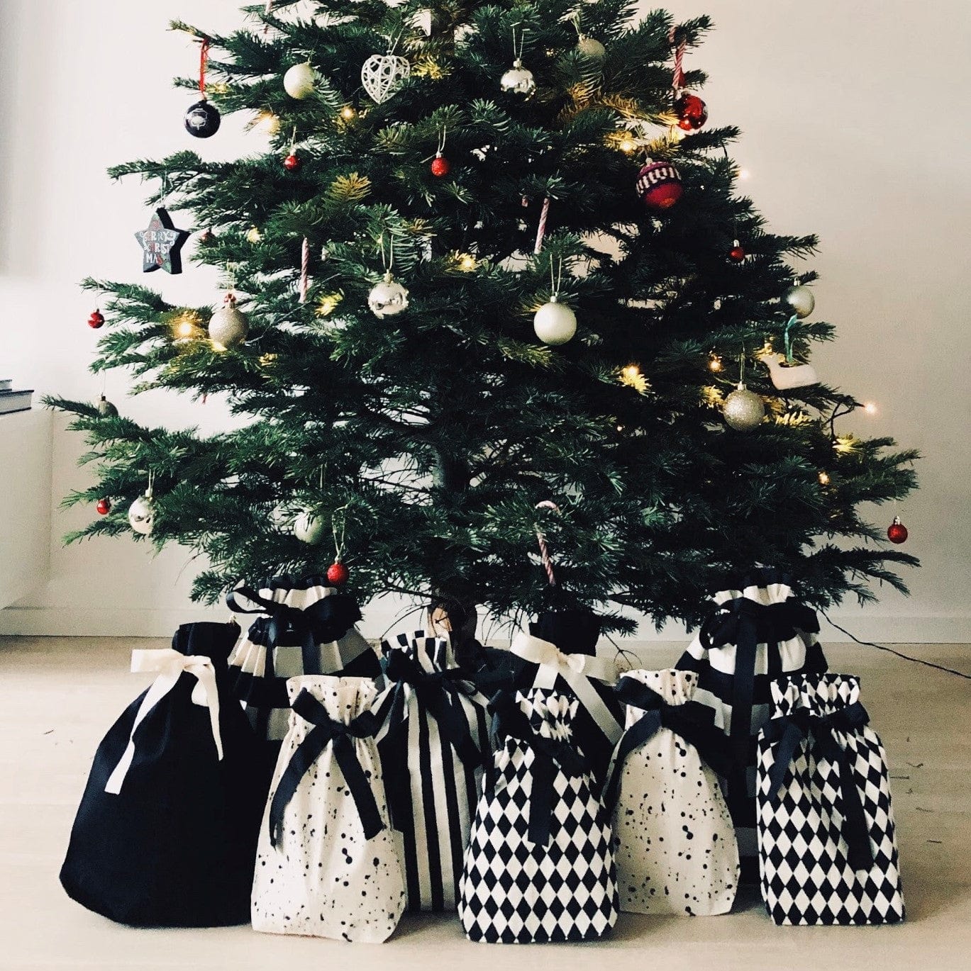 Bag-all Gift Bag Striped Medium displayed under Christmas tree alongside black and white patterned reusable gift bags, showcasing sustainable holiday gift wrapping alternatives with elegant patterns