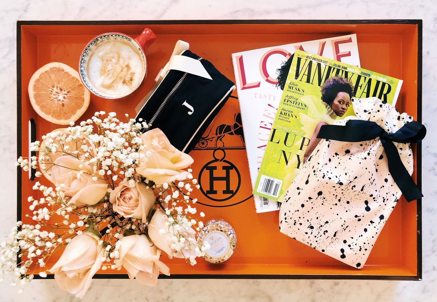 Bag-all Gift Card displayed on orange tray with peach roses, coffee cups, fashion magazines, grapefruit, and Hermes box, creating a luxurious lifestyle setting