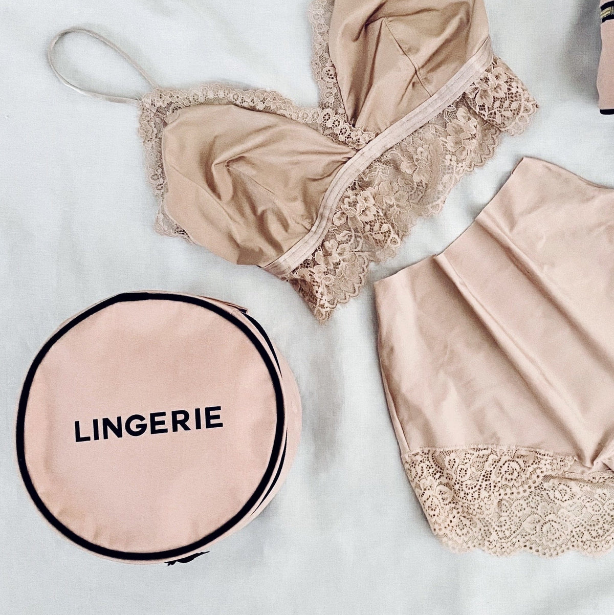 Bag-all Round Lingerie Case in blush pink with black text, shown with matching pink lace lingerie set and accessories on white background