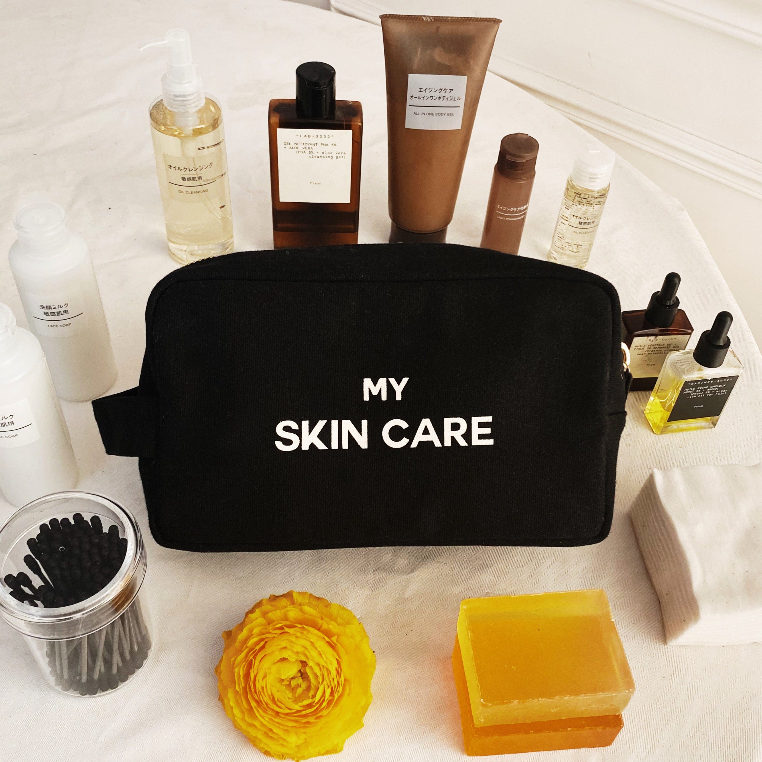 Bag-all My Skin Care black organizing pouch with waterproof lining, gold zipper displayed with skincare products, yellow flower and soap accessories