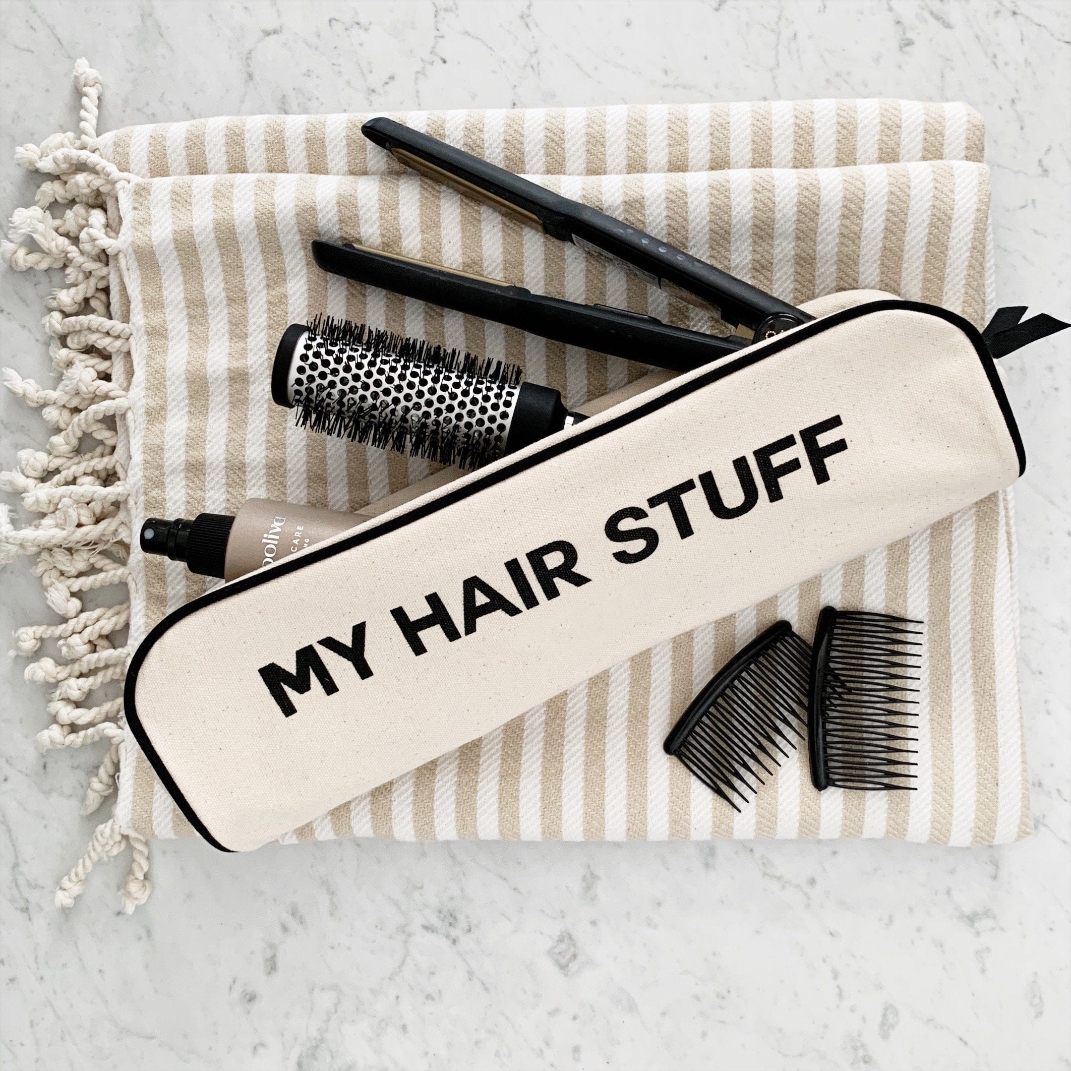Bag-all Hair Stuff Travel Case in cream with black text, shown with styling tools including brush, combs and flat iron on striped cotton background