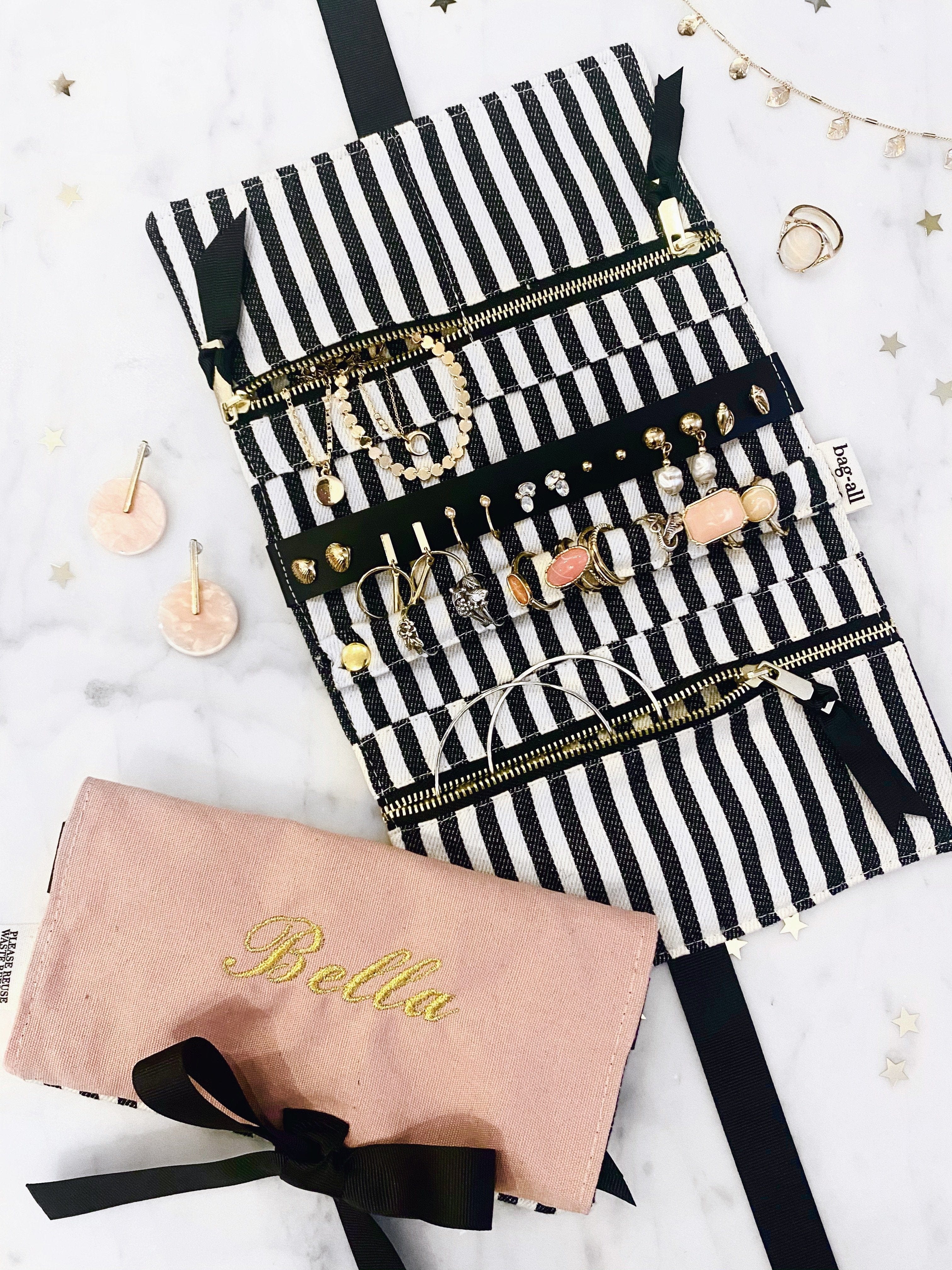 Bag-all Jewelry Organizer Travel Pouch in blush pink with striped interior, featuring multiple compartments, leather earring holder, and ring storage, displayed with jewelry pieces