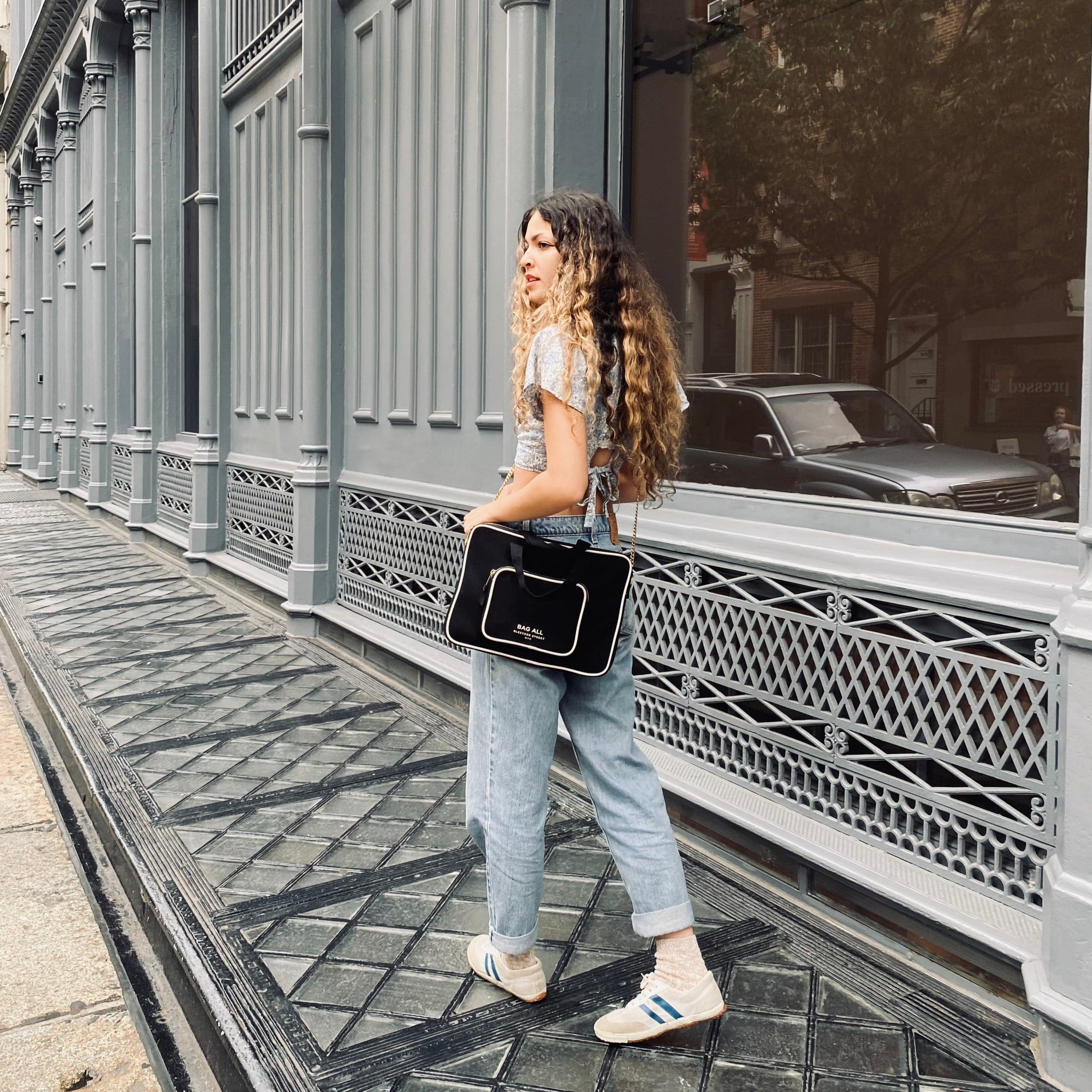 Bag-all Black Laptop Case 13" with handle and charger pocket shown in urban setting, featuring padded protection, front storage, and double carrying handles. Perfect for modern professionals and students.