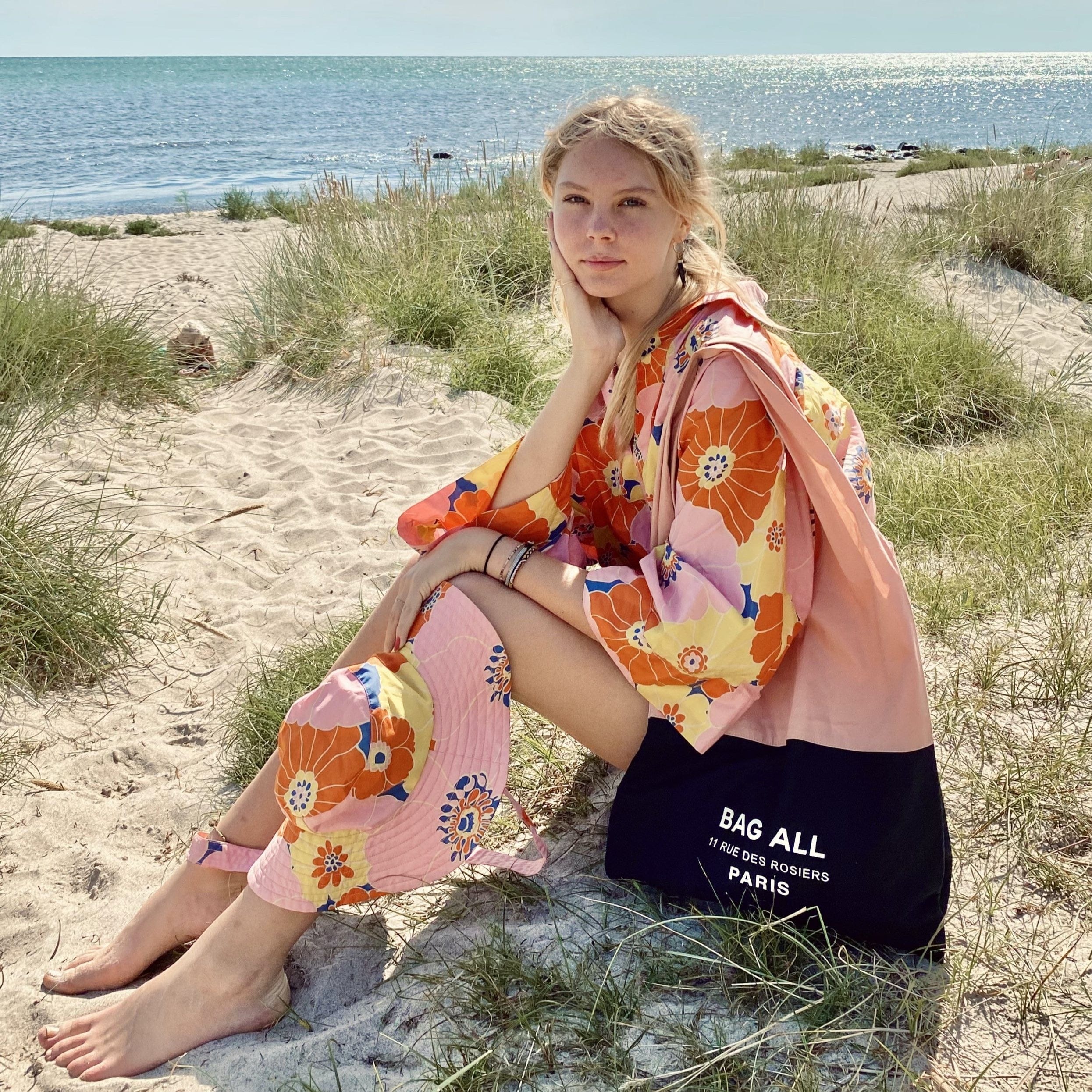 A girl at the beach with her pink and black tote bag.