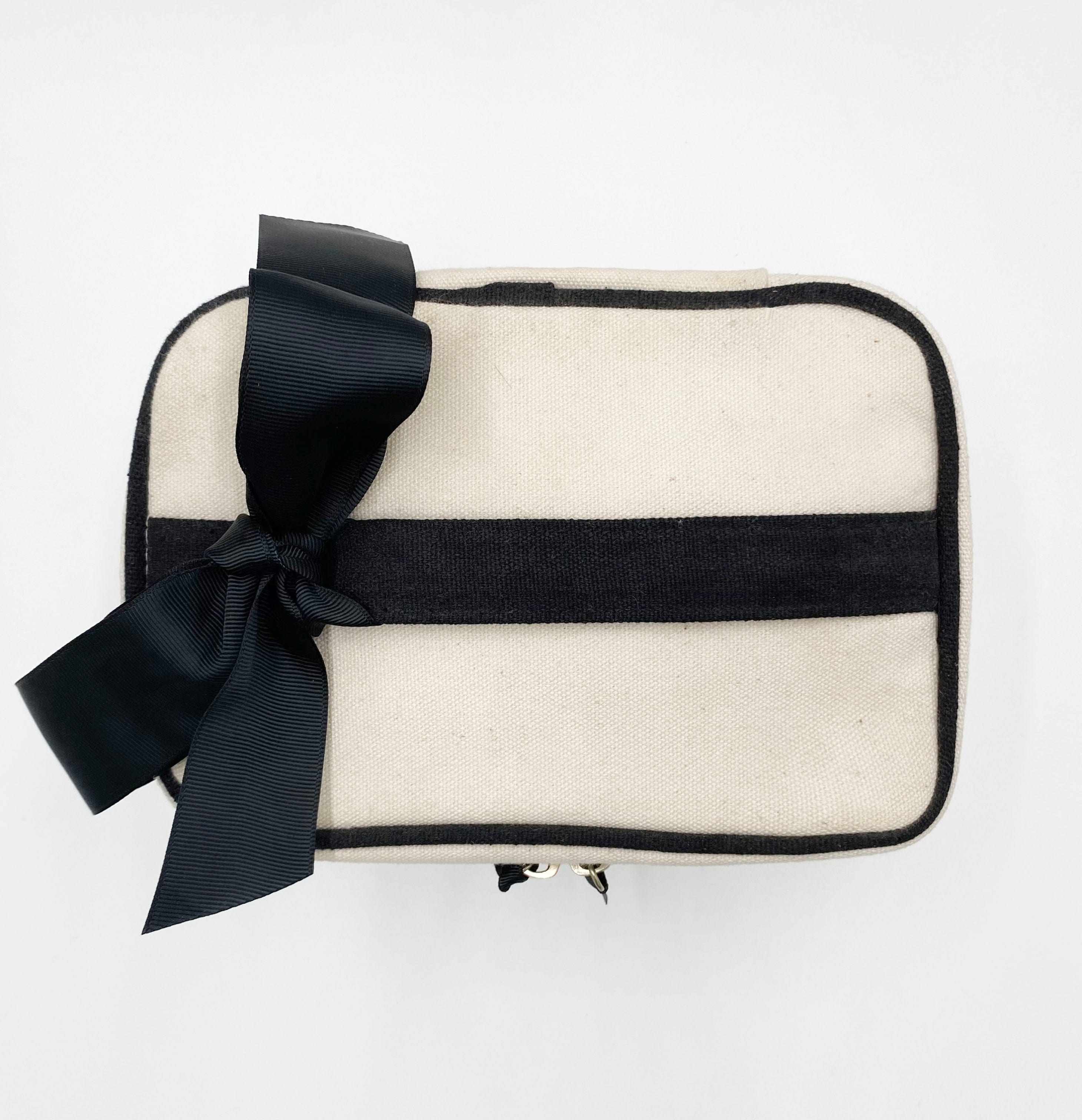 Bag-all Vitamins Storage and Travel Box in cream canvas with black trim and bow, featuring waterproof lining and compact square design for organized supplement storage