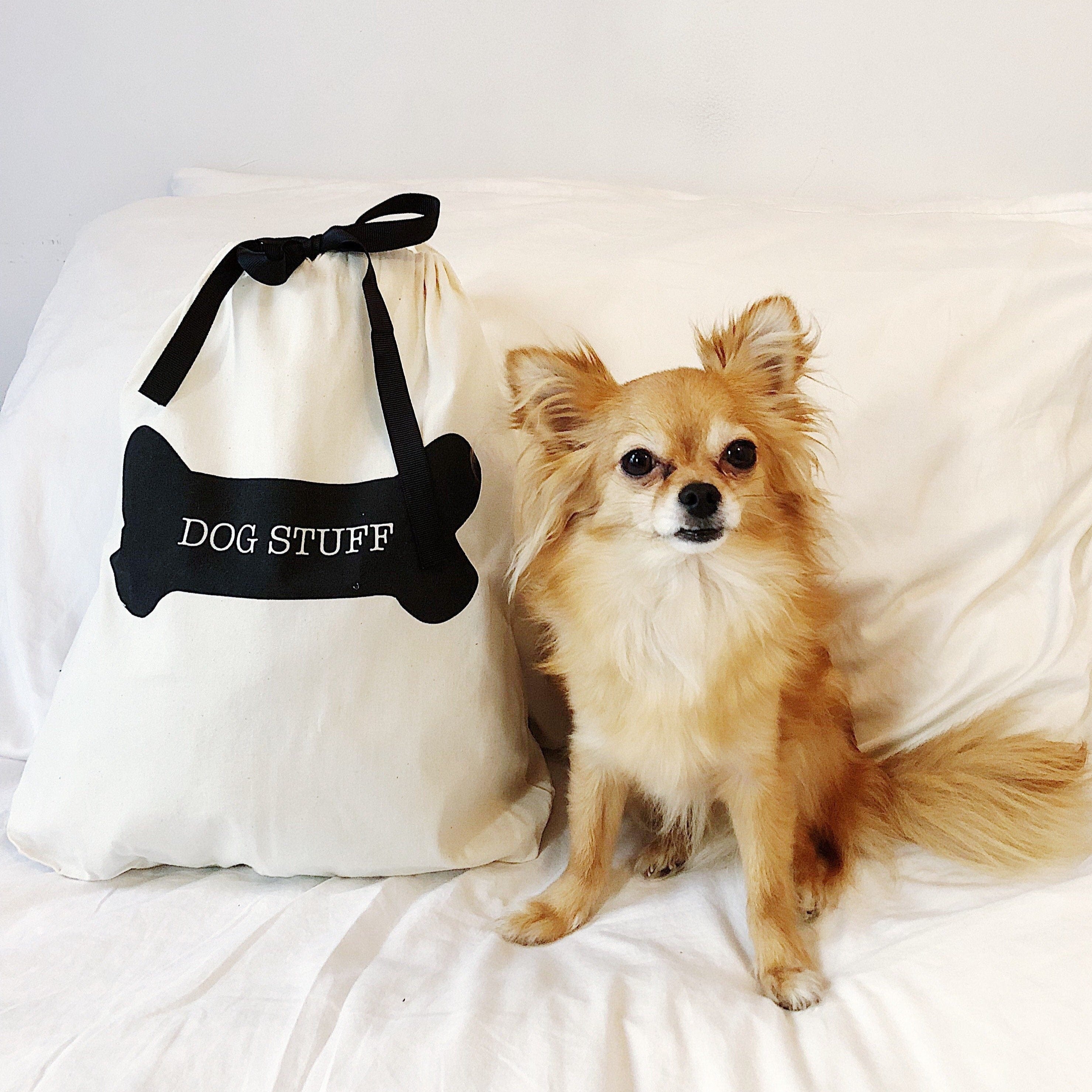 Bag-all cream Dog Stuff Bag with black bone design shown with small Chihuahua mix on white bedding. Stylish pet accessory storage solution with ribbon tie closure.