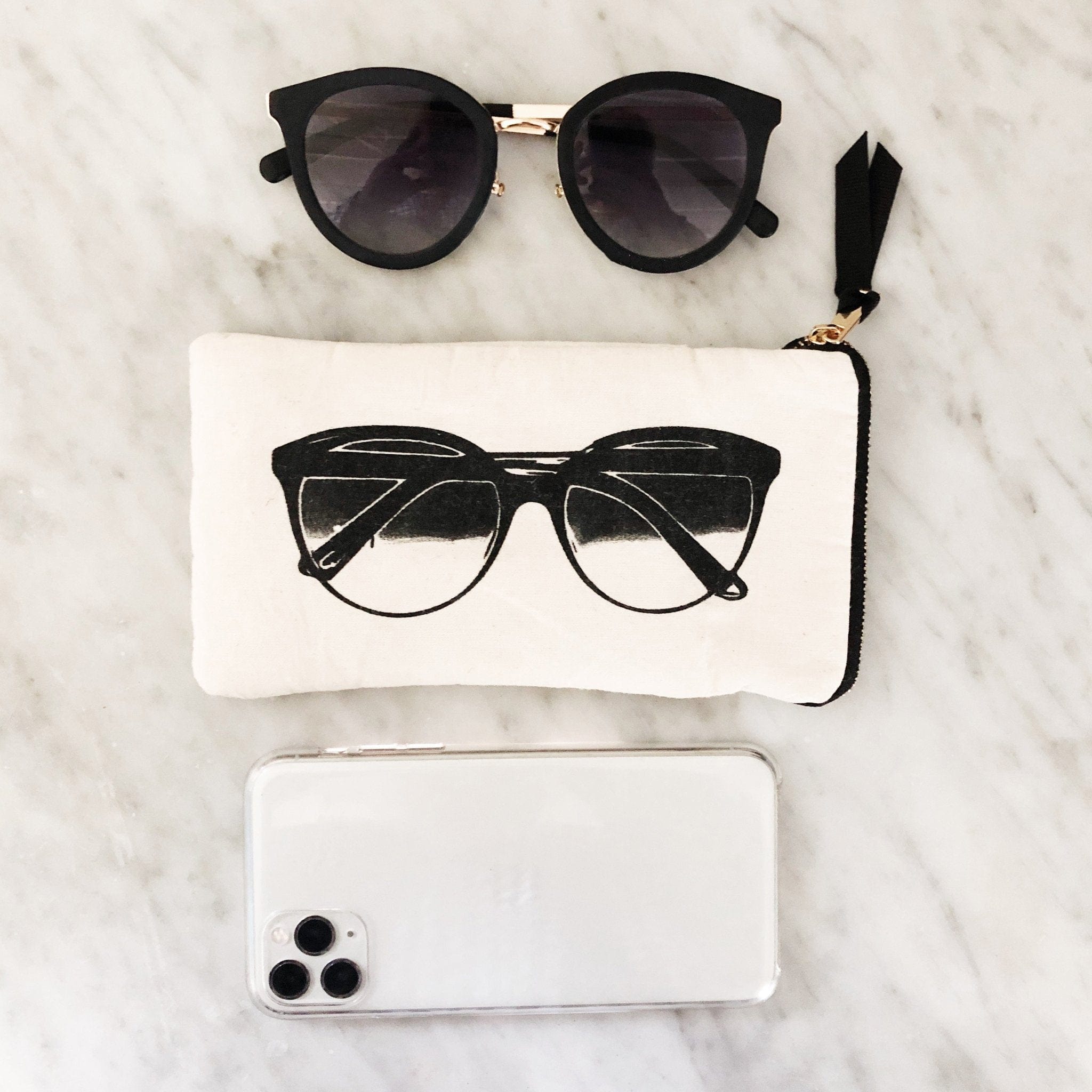 Bag-all Glasses Case with Outside Pocket in Cream featuring black sunglasses print, zipper closure and functional exterior pocket on marble surface with matching sunglasses