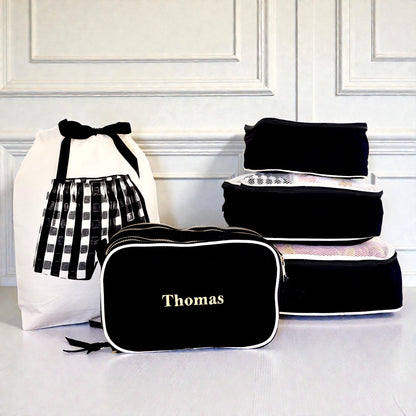 Black personalized travel organizer and 5-pack packing cubes by Bag-all stacked beside white laundry bag with bow detail