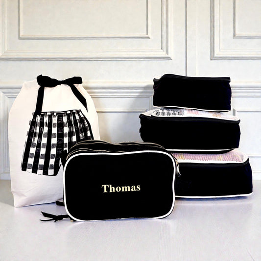 Black personalized travel organizer and 5-pack packing cubes by Bag-all stacked beside white laundry bag with bow detail