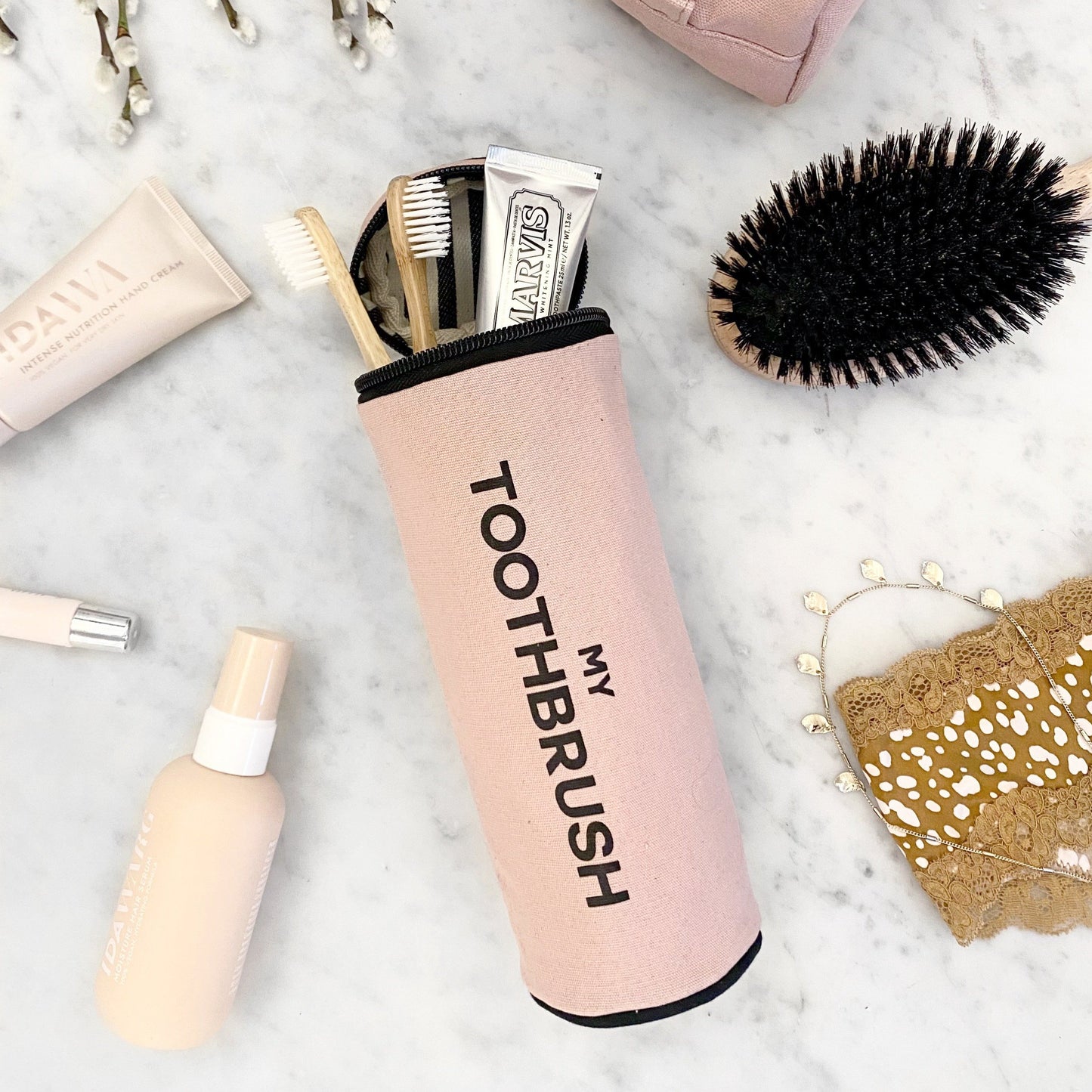 Bag-all pink blush toothbrush organizer with zipper holding travel toothbrushes and toothpaste on marble surface