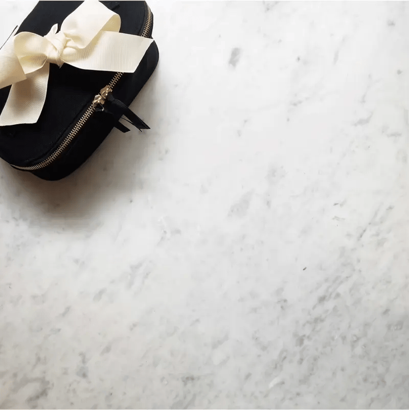 Bag-all black travel case with elegant cream bow and gold zipper detail on luxurious marble background