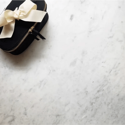 Bag-all black travel case with elegant cream bow and gold zipper detail on luxurious marble background