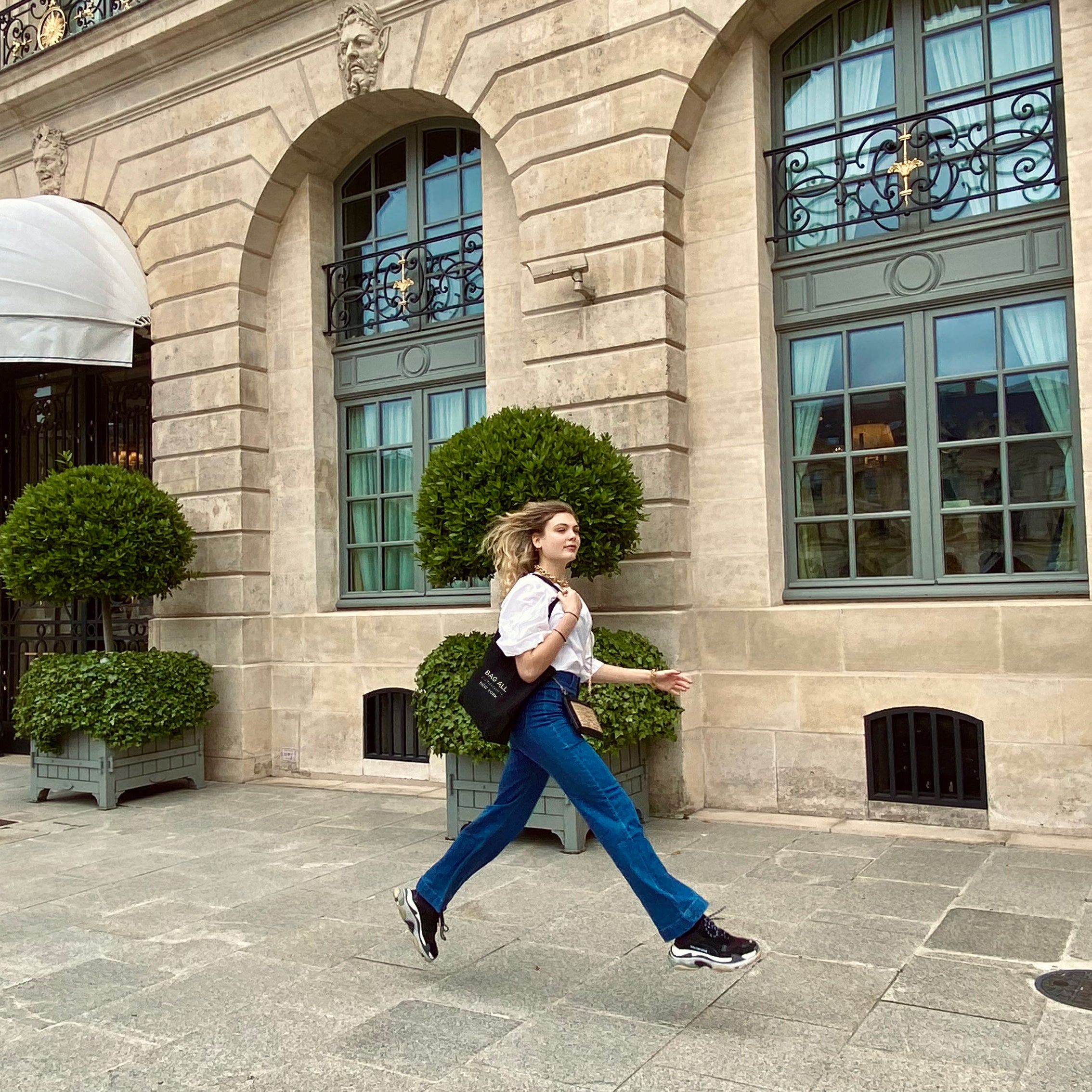 Woman striding past elegant Parisian building wearing Bag-all New York City Tote with Zipper and Inside Pocket in Black, showcasing its versatile urban style against classic architecture