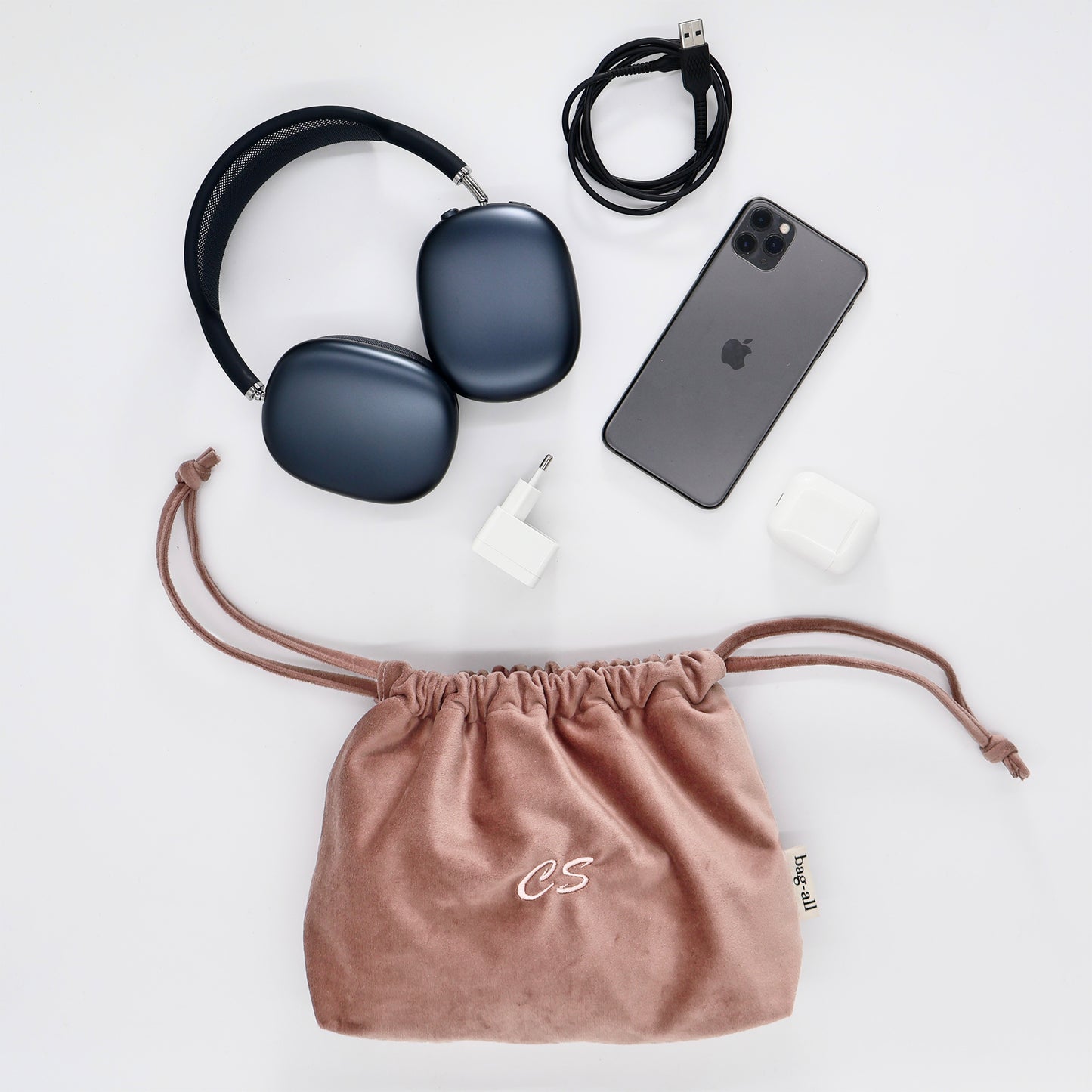 Pink velvet drawstring tech pouch by Bag-all with headphones, charger, phone, and AirPods for organized storage