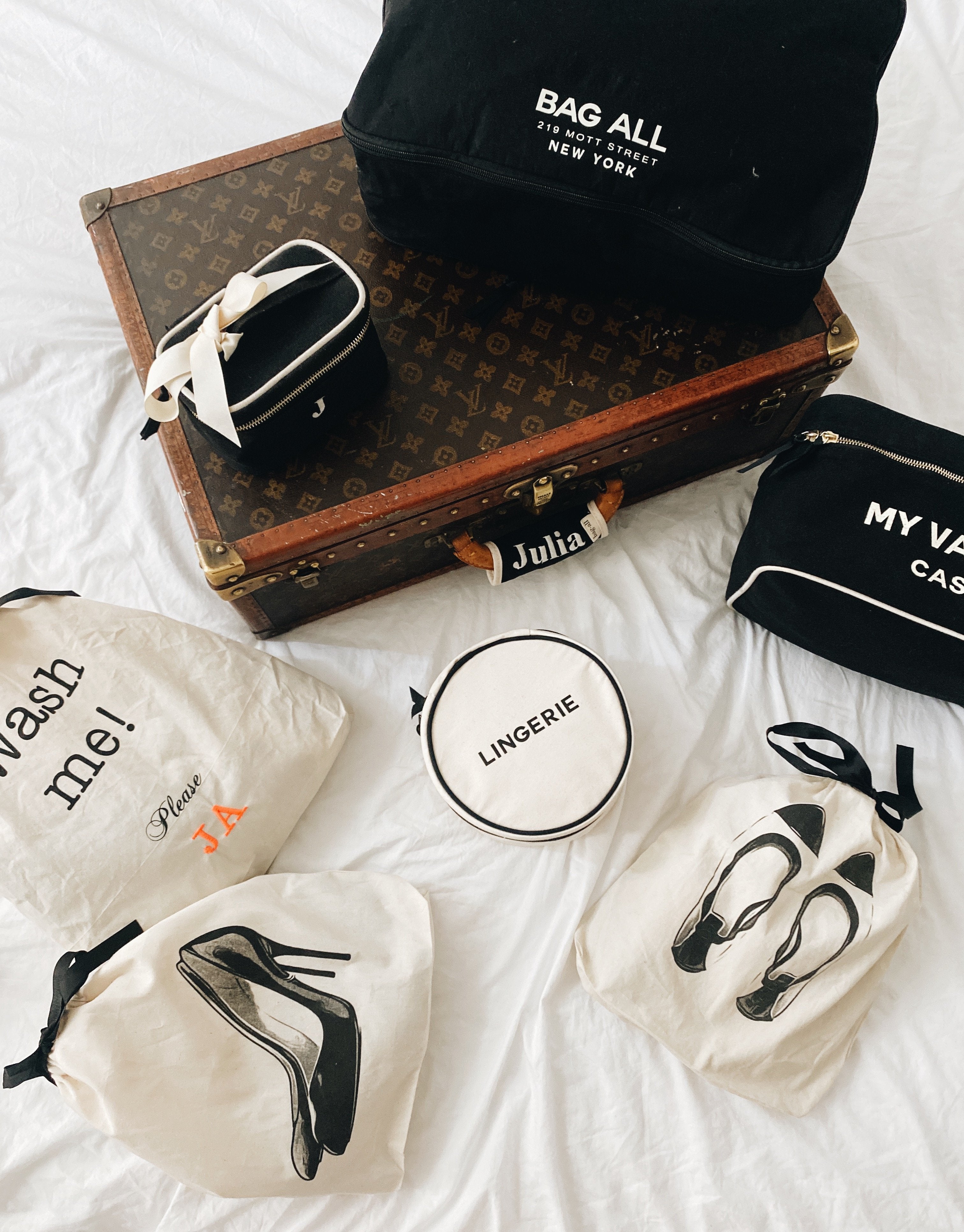 Bag-all Luggage Handle Cover displayed with vintage Louis Vuitton trunk and travel organizing bags featuring shoe and lingerie cases in black and white canvas, showcasing luxury travel accessories