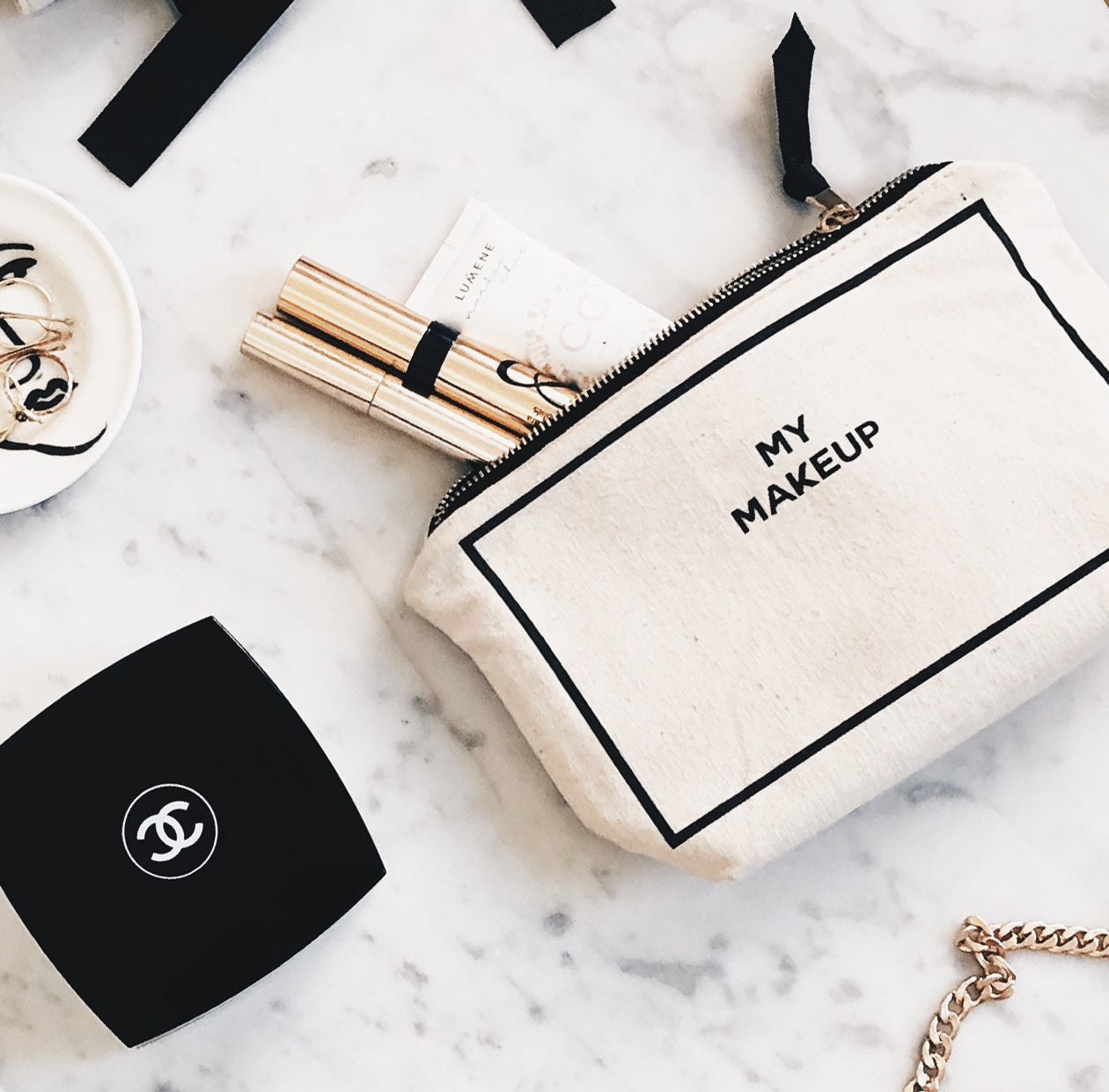 Cream canvas makeup pouch with black border and text MY MAKEUP from Bag-all on marble surface with cosmetics nearby