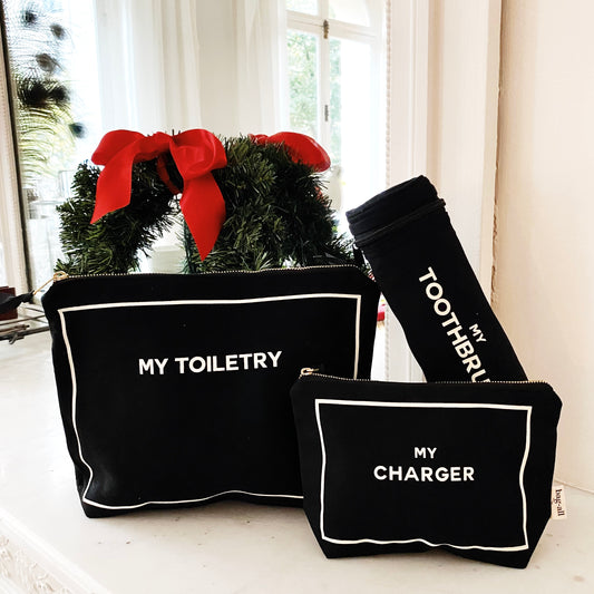 Bag-all black three-pack gift set with My Toiletry, My Charger, and My Toothbrush cases near wreath with red bows
