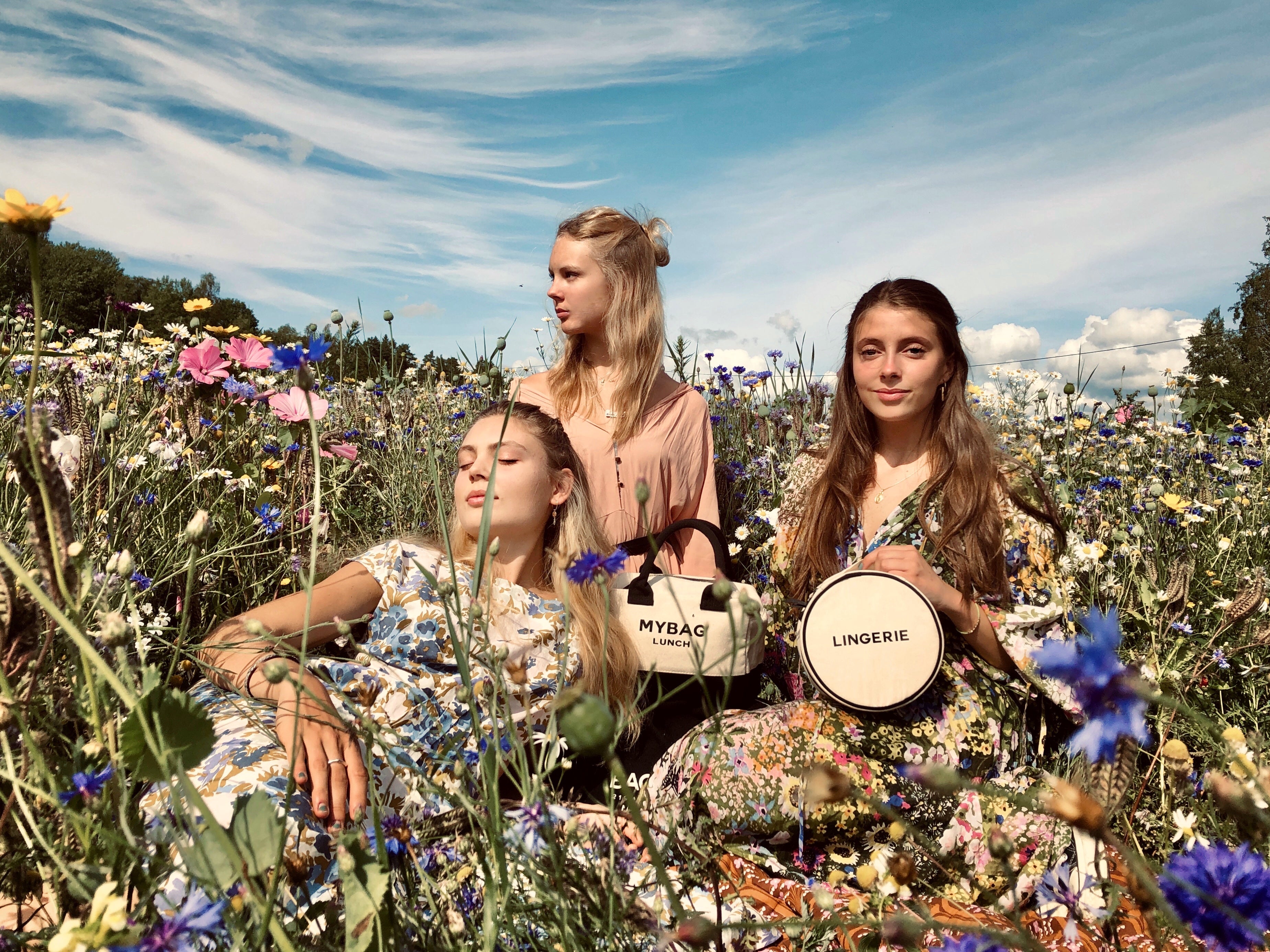 Three women in floral dresses sitting in wildflower field holding Bag-all canvas storage bags gallery position 1