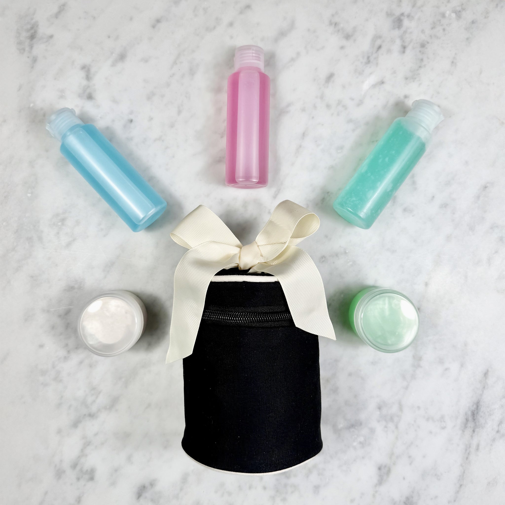 Black Bag-all travel organizer with bow and colorful travel bottles and jars on marble surface