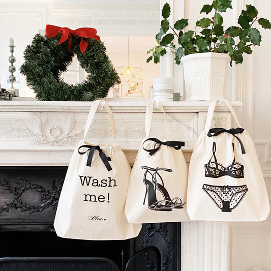 Three cream Bag-all tote bags with black bows and shoe, lingerie, and "Wash me!" prints hanging on mantel with Christmas wreath