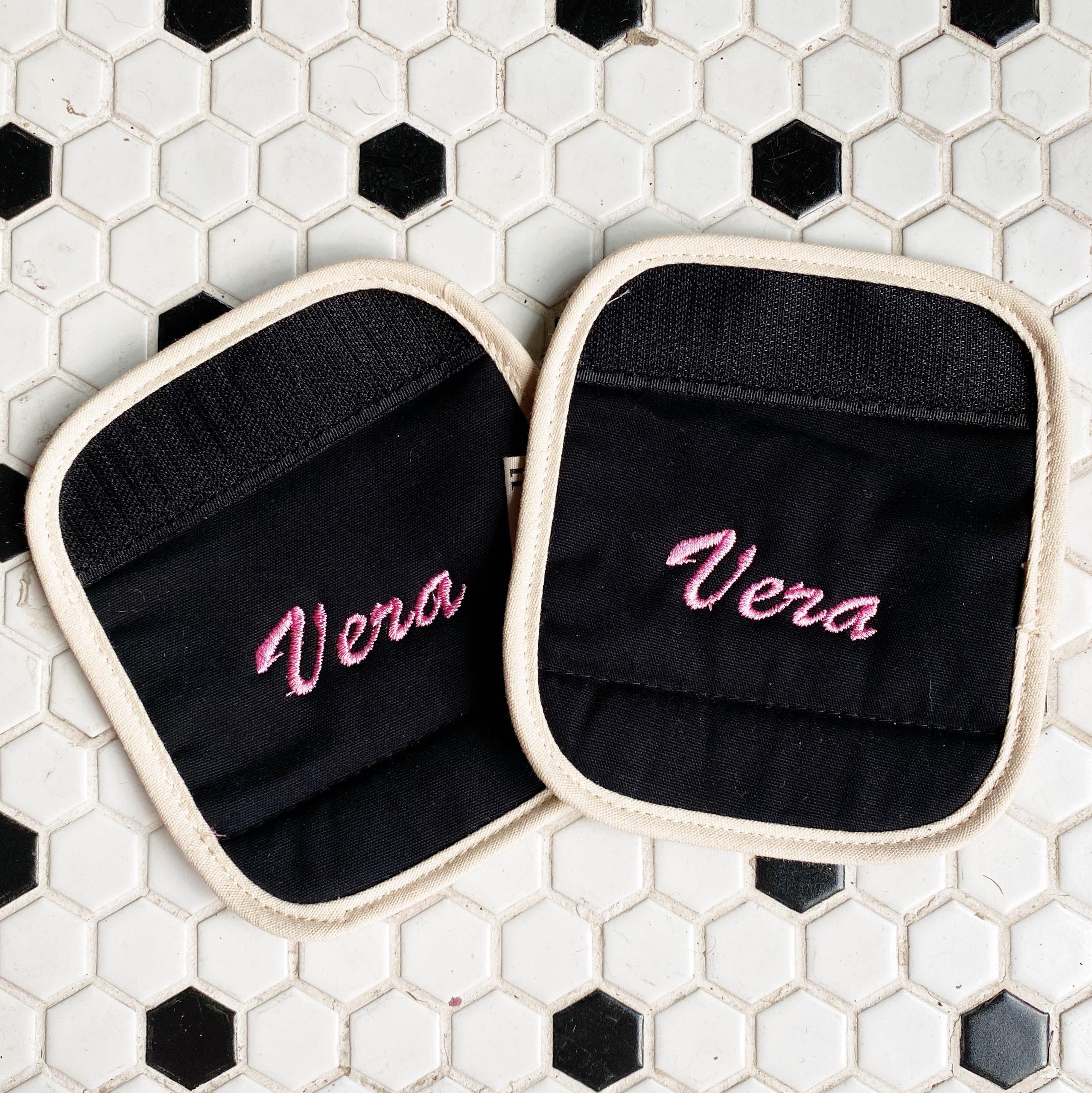 Bag-all Luggage Handle Cover in black cotton with cream trim featuring 'Vera' custom pink embroidery monogram on hexagonal tile background, perfect for personalized travel accessory