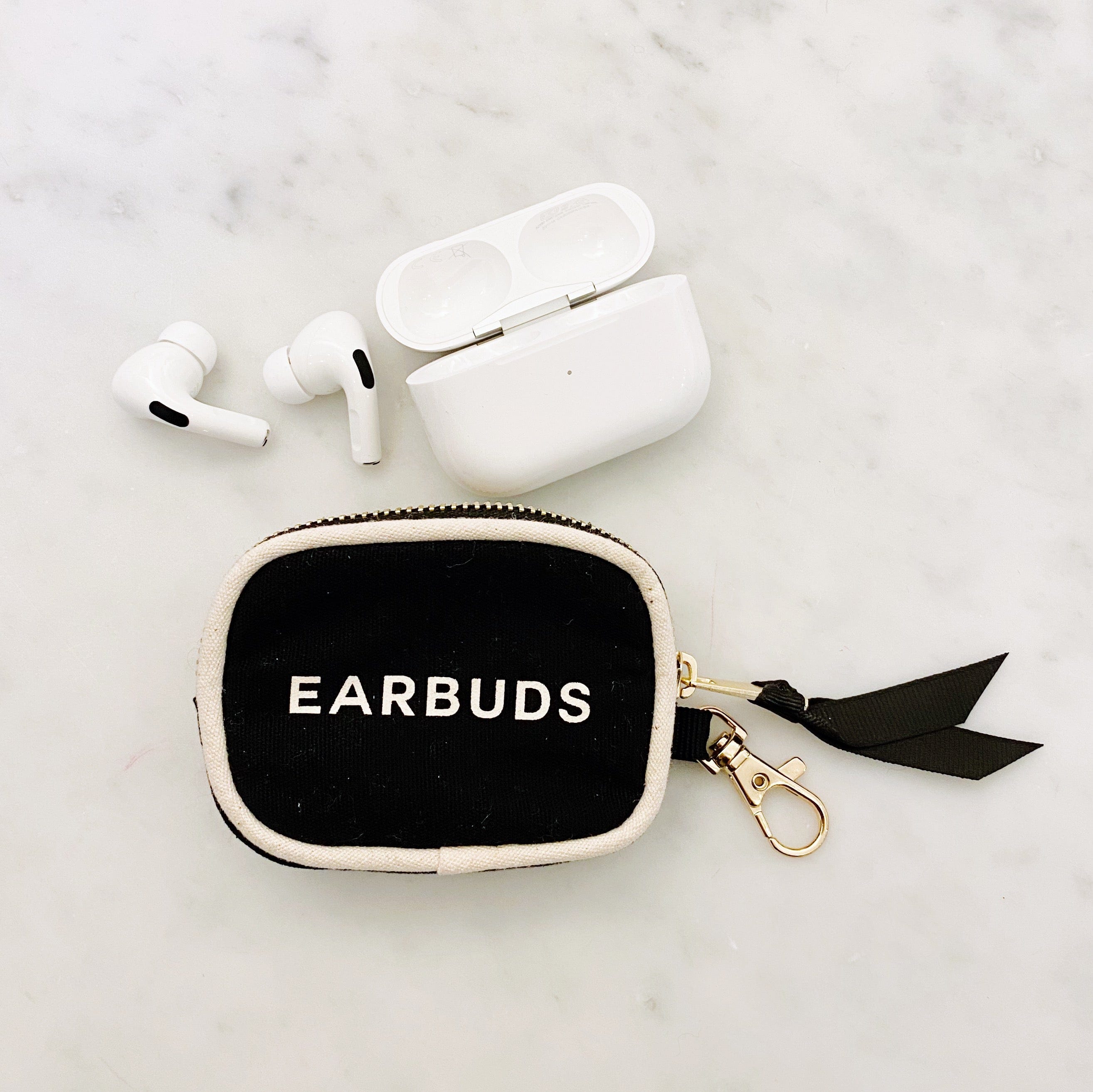 Bag-all Black Earbuds Case with wireless earphones and charging case, featuring elegant black cotton fabric, gold zipper, and bow detail on marble background