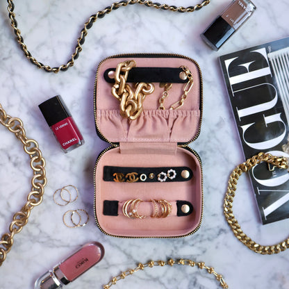 Pink velvet Bag-all Cute Jewelry Box open with gold chains, earrings, and rings on marble with cosmetics nearby