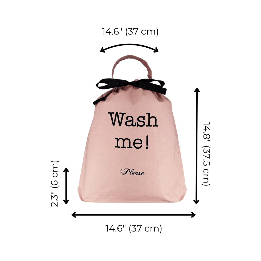 Bag-all pink laundry bag with 'Wash me!' text in black, featuring black bow handle and measurements displayed. Stylish organizer for travel and home use.