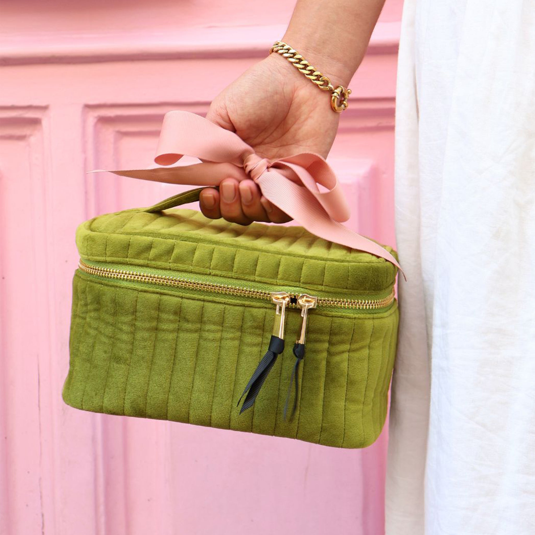 Green quilted velvet cosmetic box with gold zipper and pink ribbon, held by hand, Bag-all organizer for makeup storage