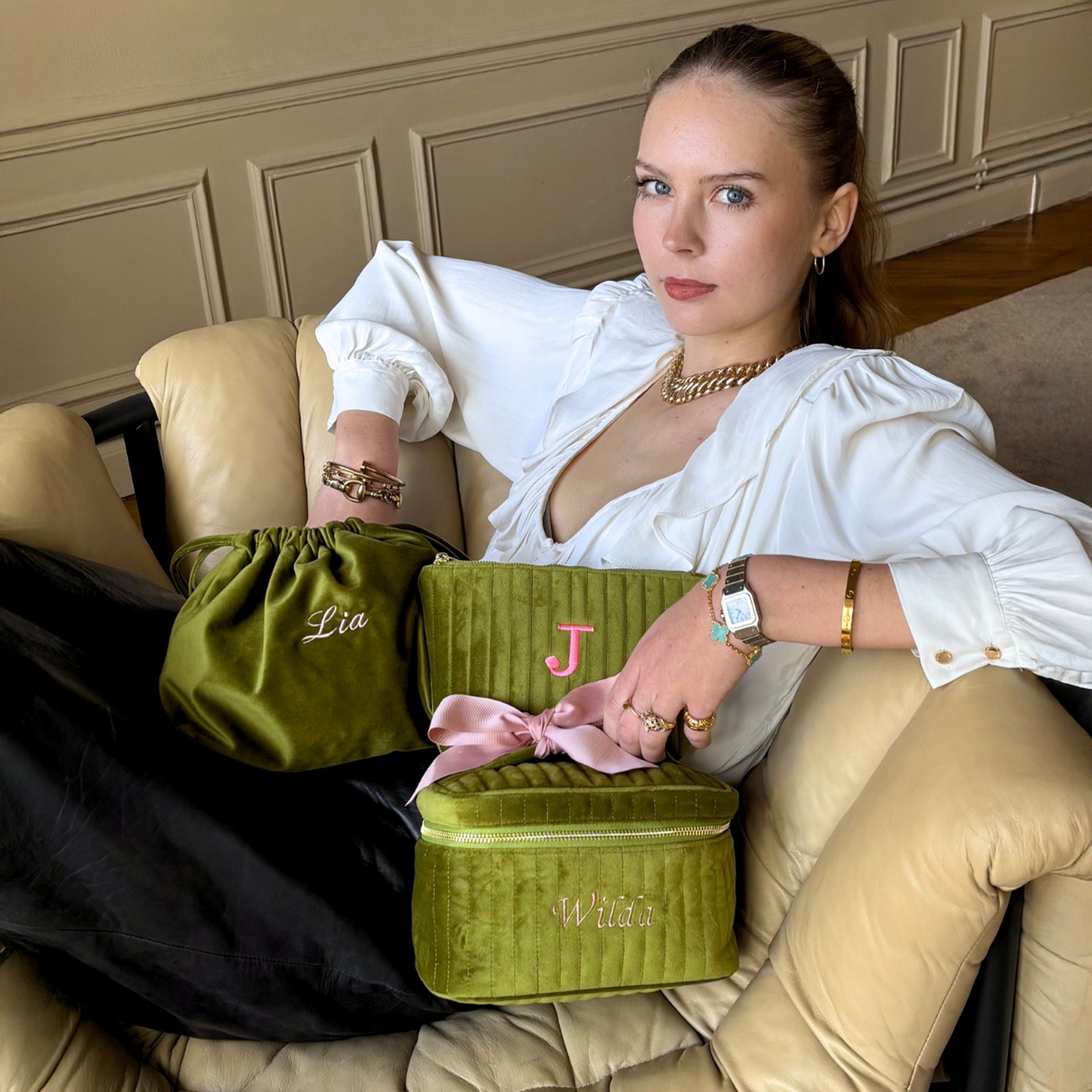Woman lounging on beige chair with three personalized green velvet Bag-all pouches gallery position 1