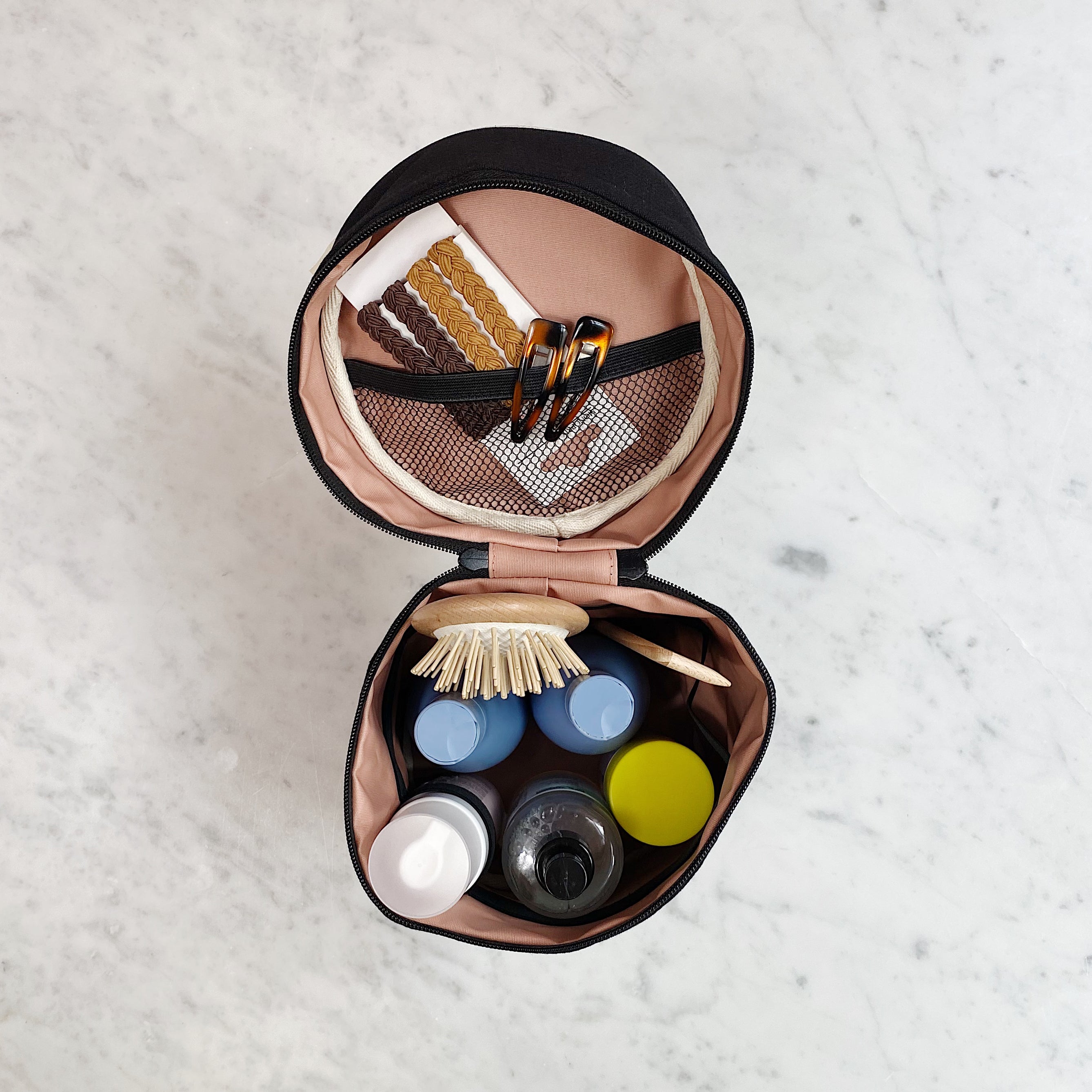 Bag-all Roomy Travel Essentials Case opened to display organized interior with mesh pocket, coated lining, and storage compartments holding various toiletries and beauty products in black and blush pink design