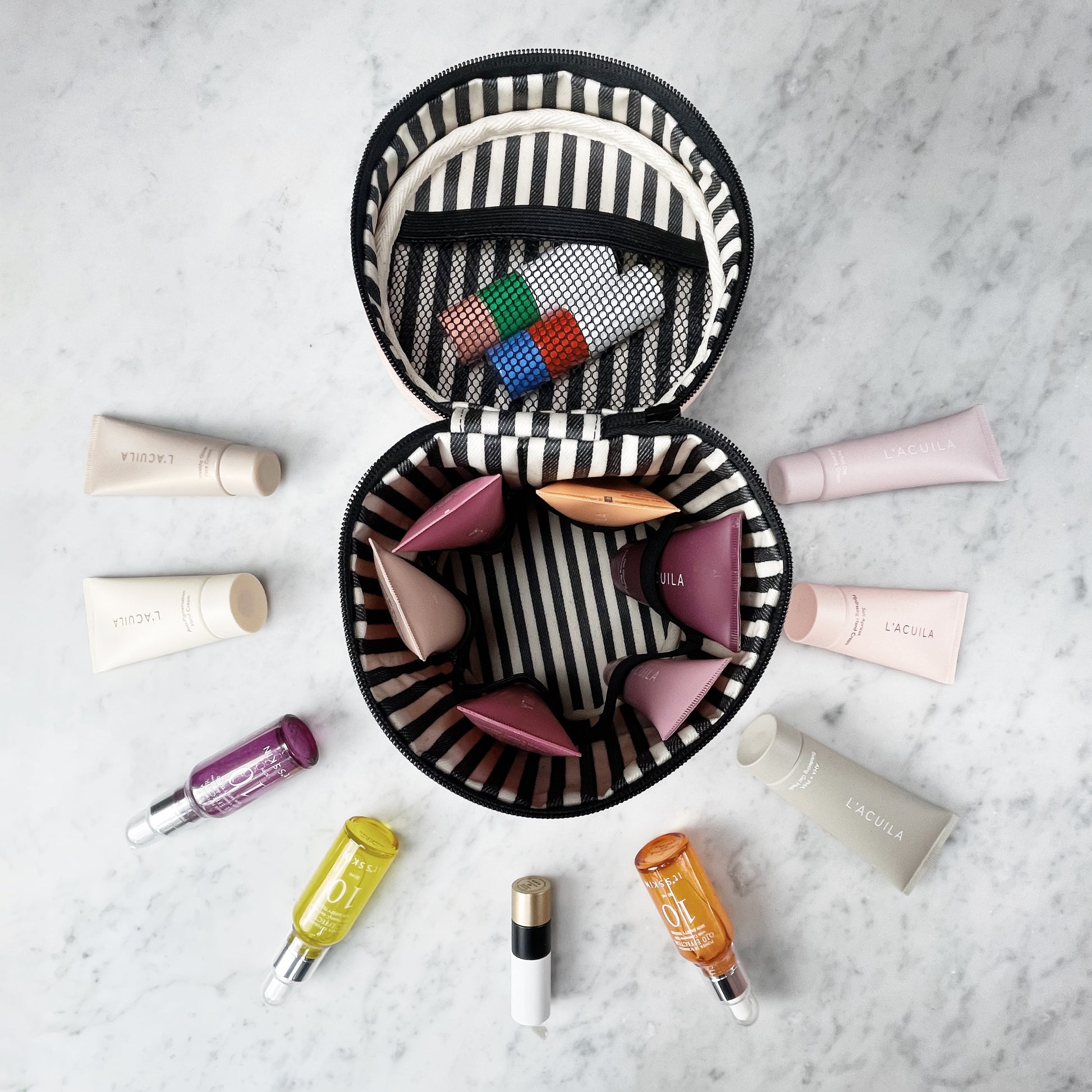 Bag-all Round My Skin Care Case in cream featuring striped interior, mesh pocket and organized compartments for skincare products, displayed with beauty essentials